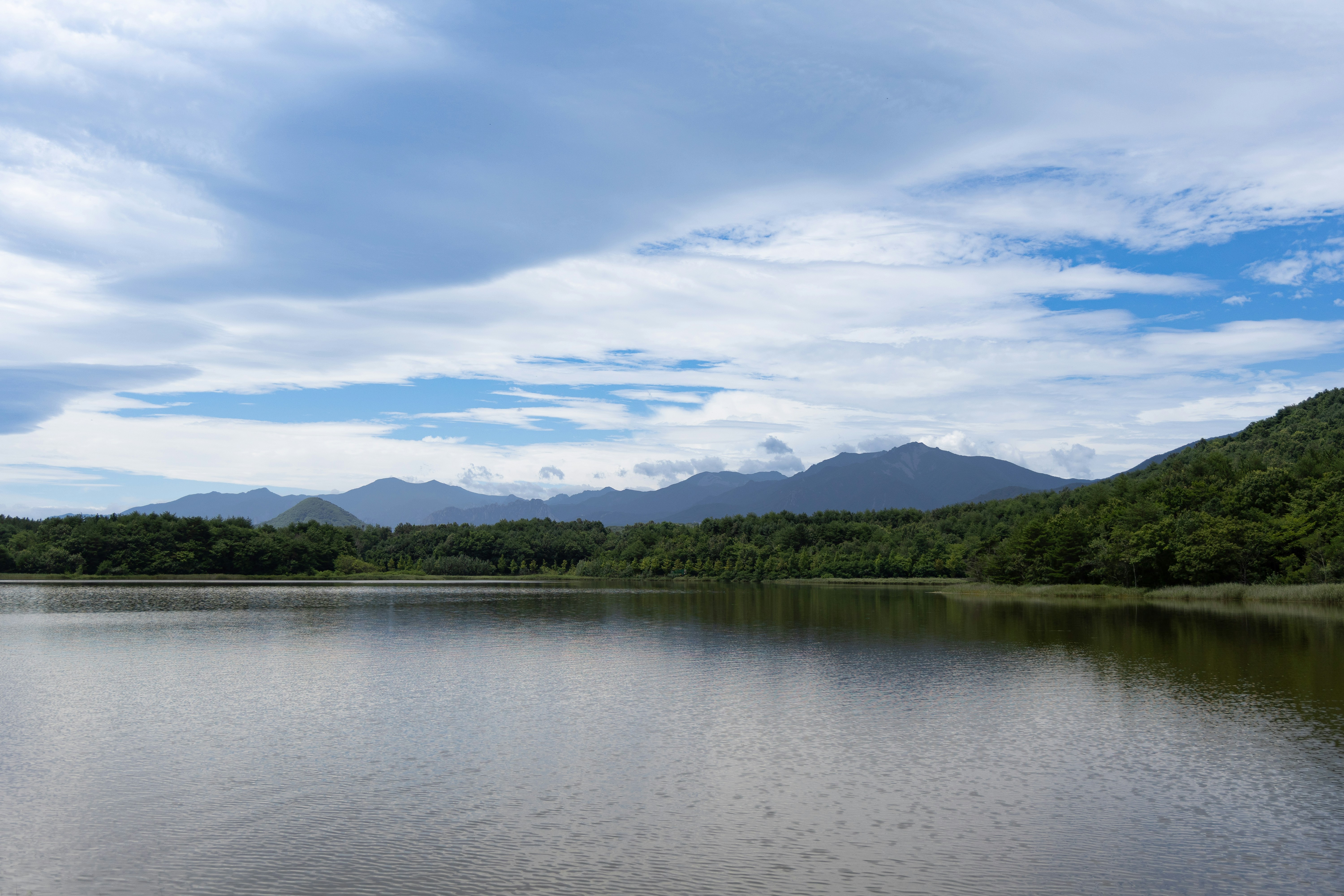 A calm lake reflects cloudy sky and green mountains