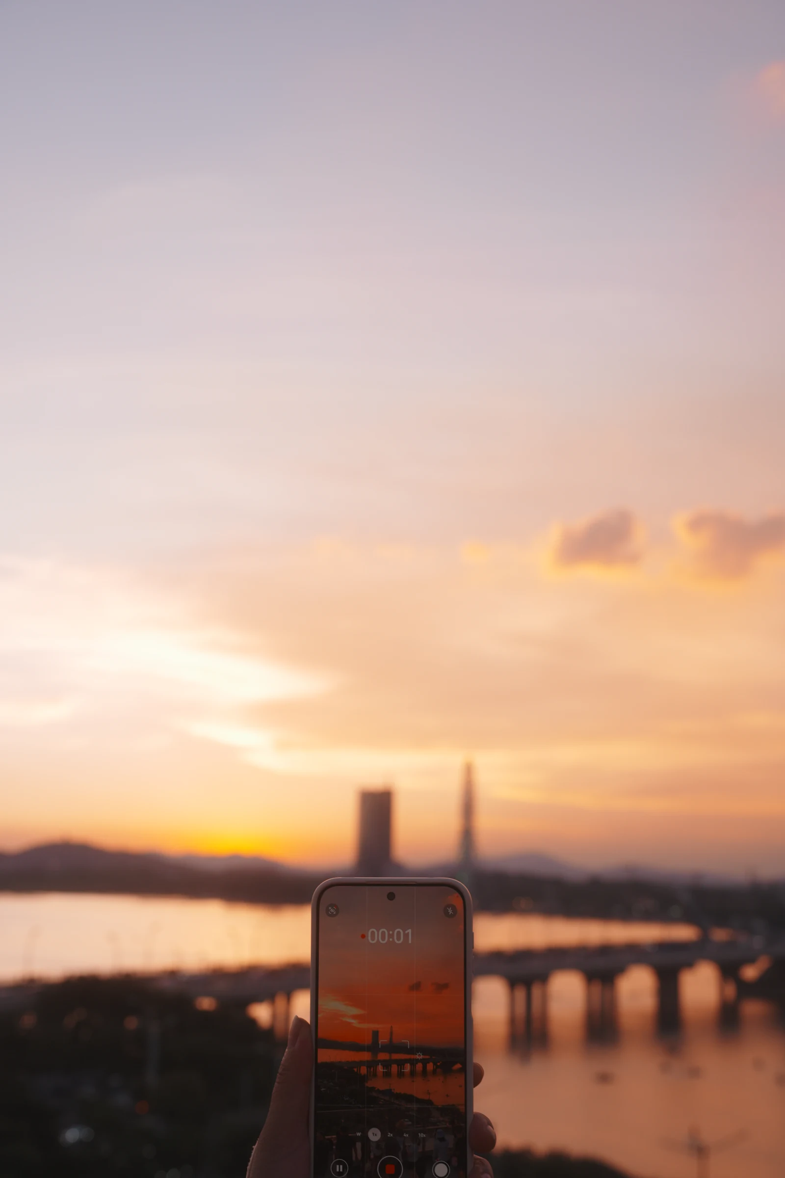 Phone held up to photograph a city skyline and river at sunset while connected to 5G abroad