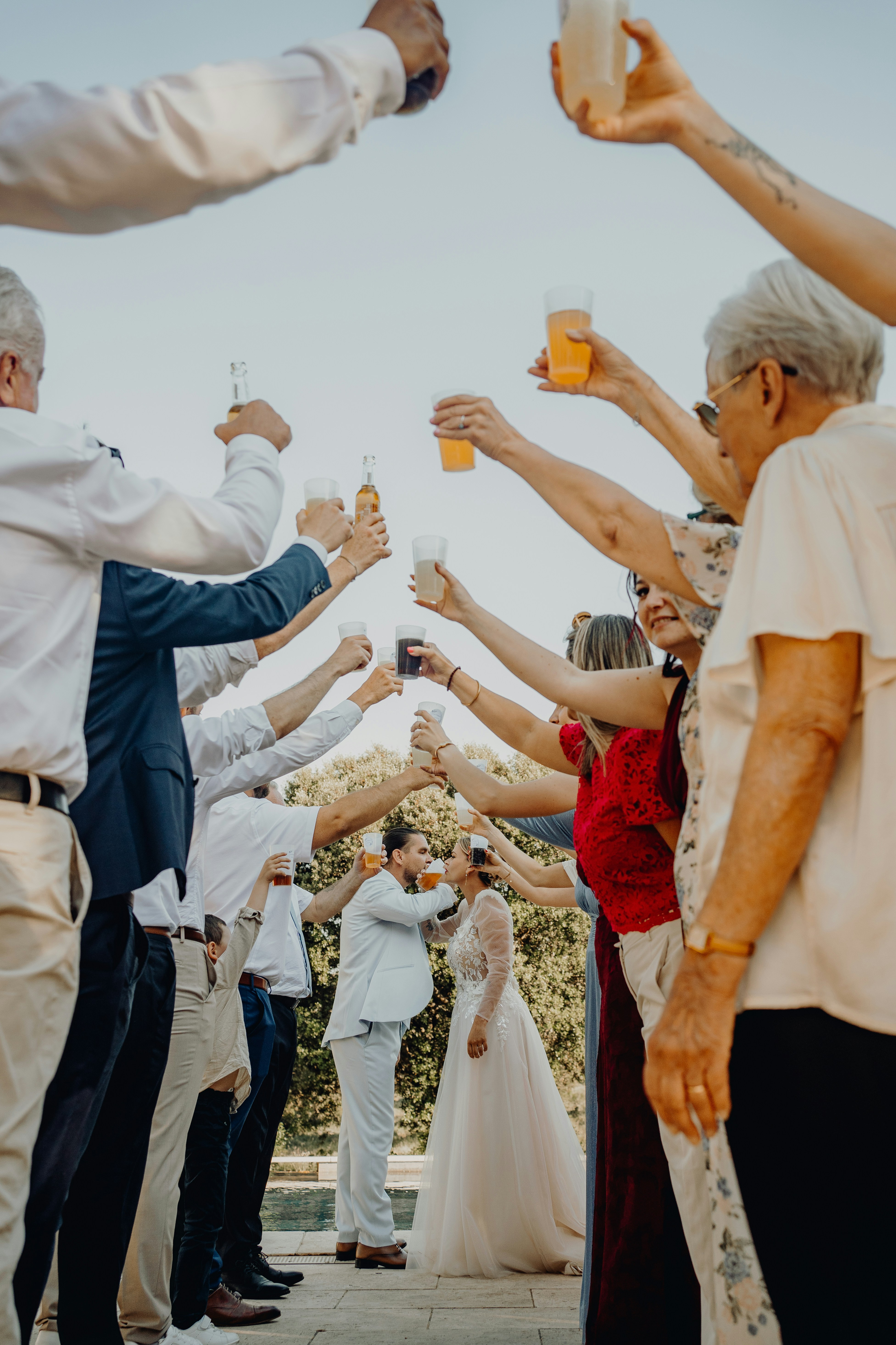 Wedding guests toast the kissing couple with raised drinks.