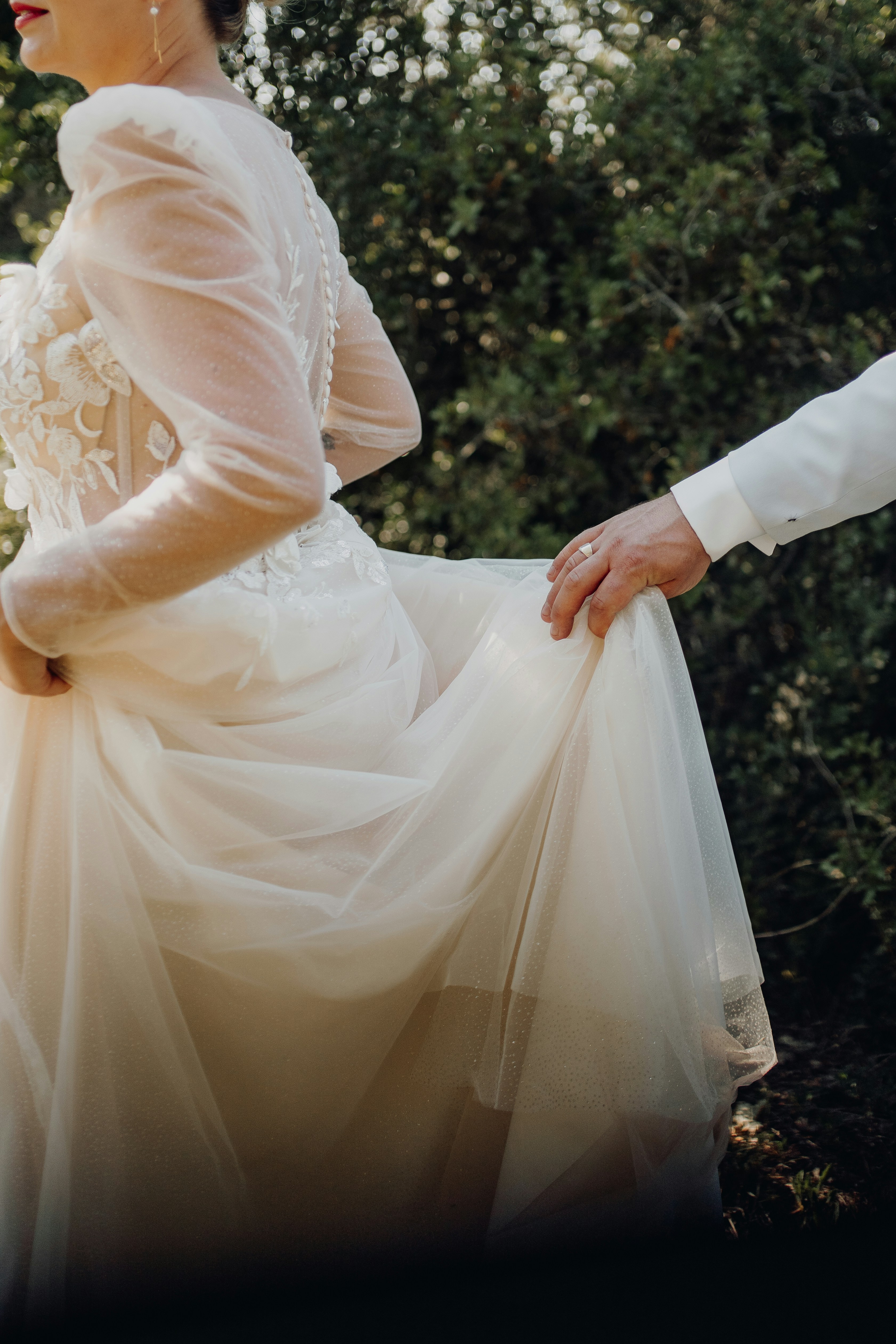 Tangan pengantin pria dengan lembut mengangkat gaun pengantin wanita di alam