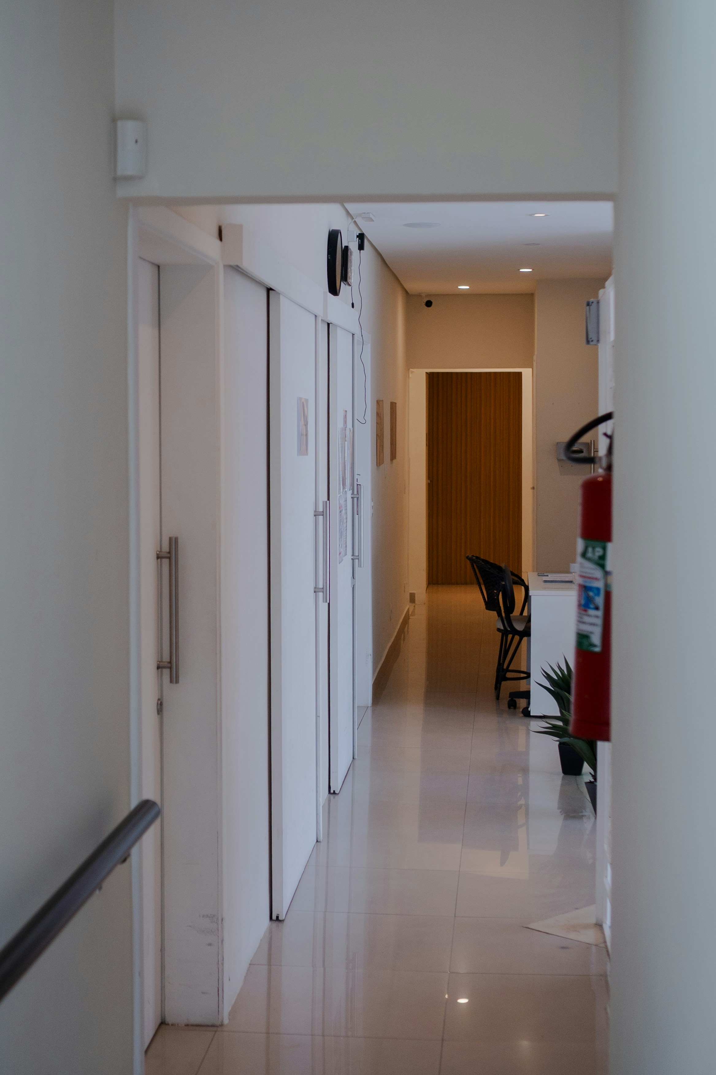 White hallway with doors, desk, and fire extinguisher.