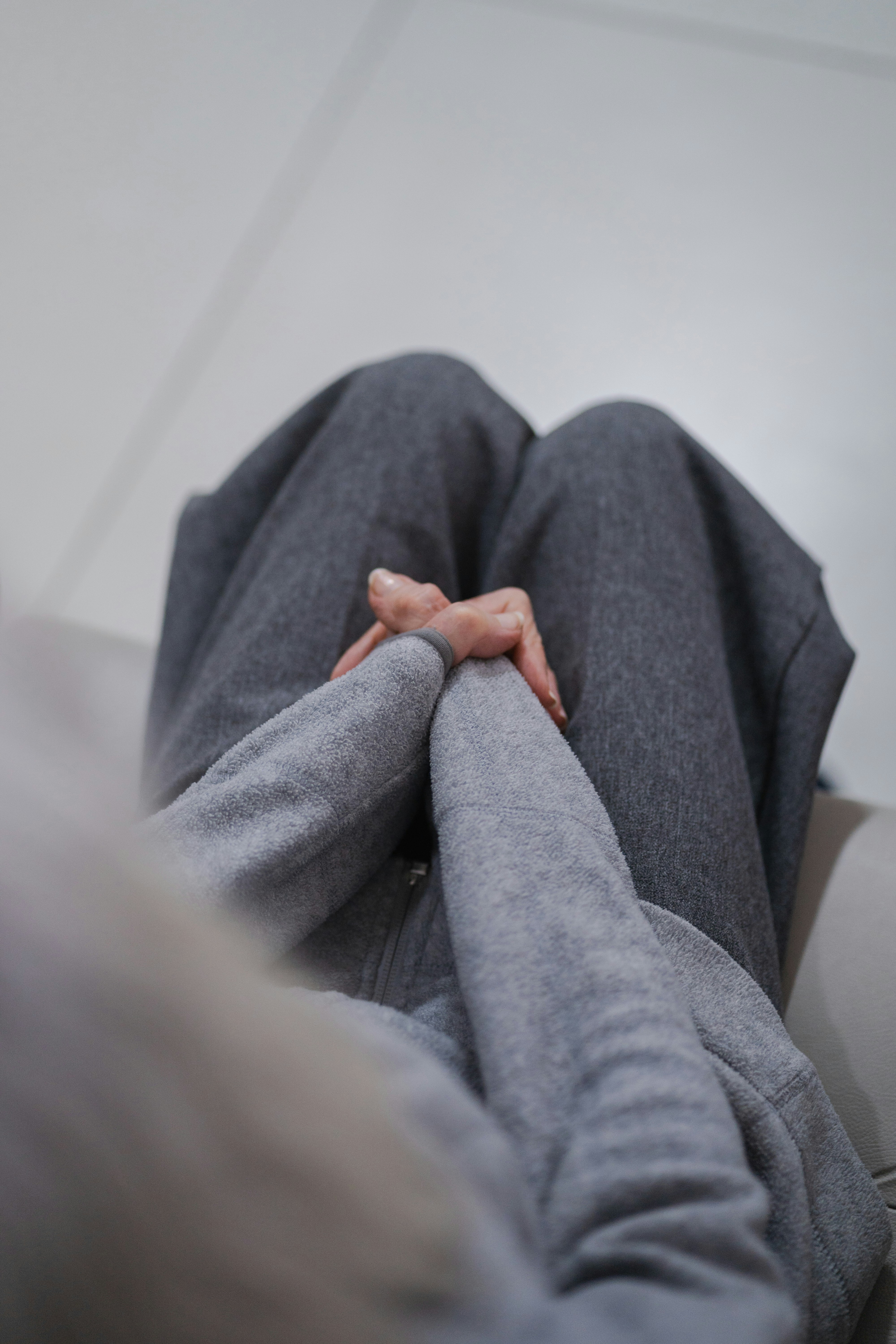 Person hiding face with grey fabric, hands clasped.