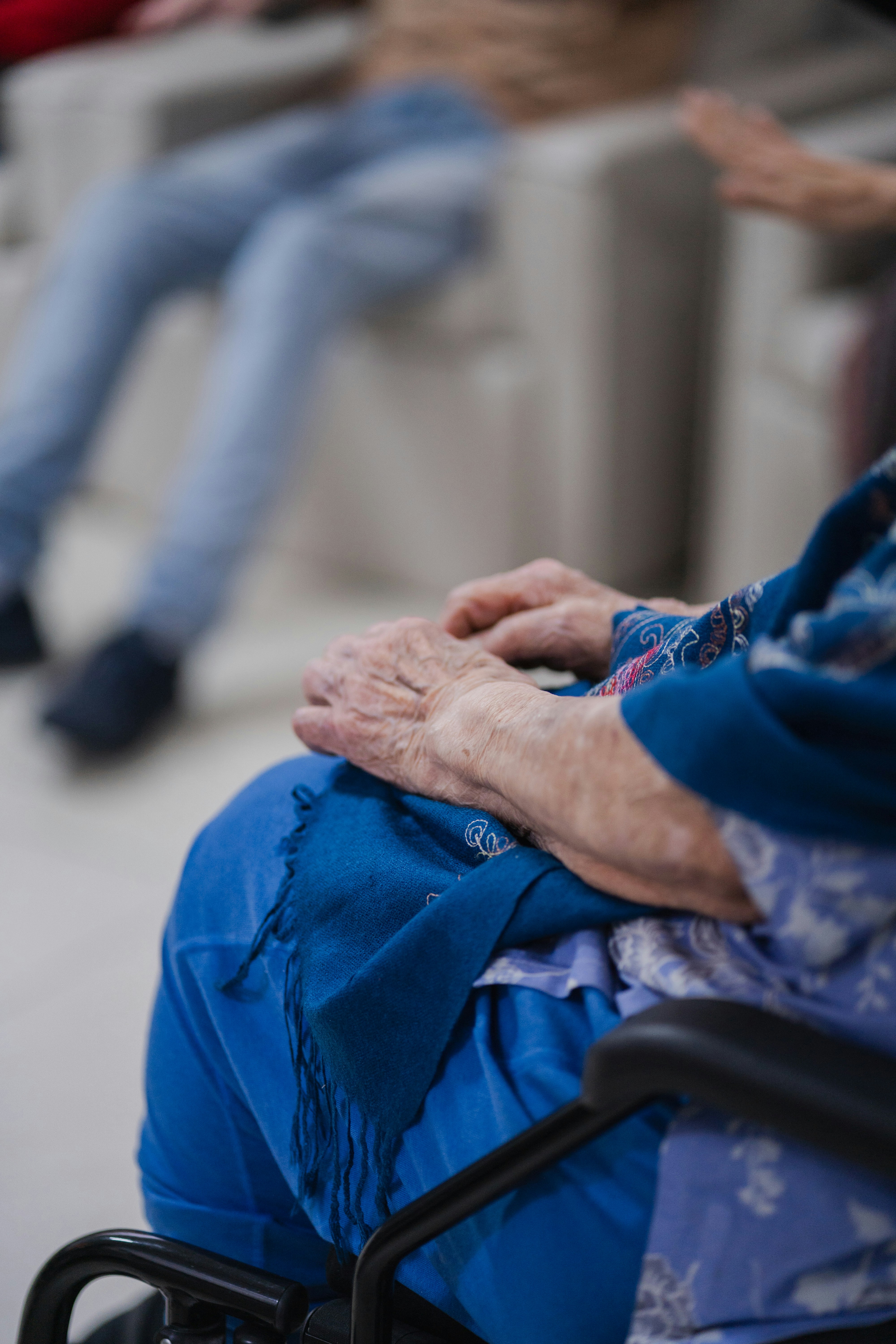 Elderly hands resting on a blue lap in a wheelchair.