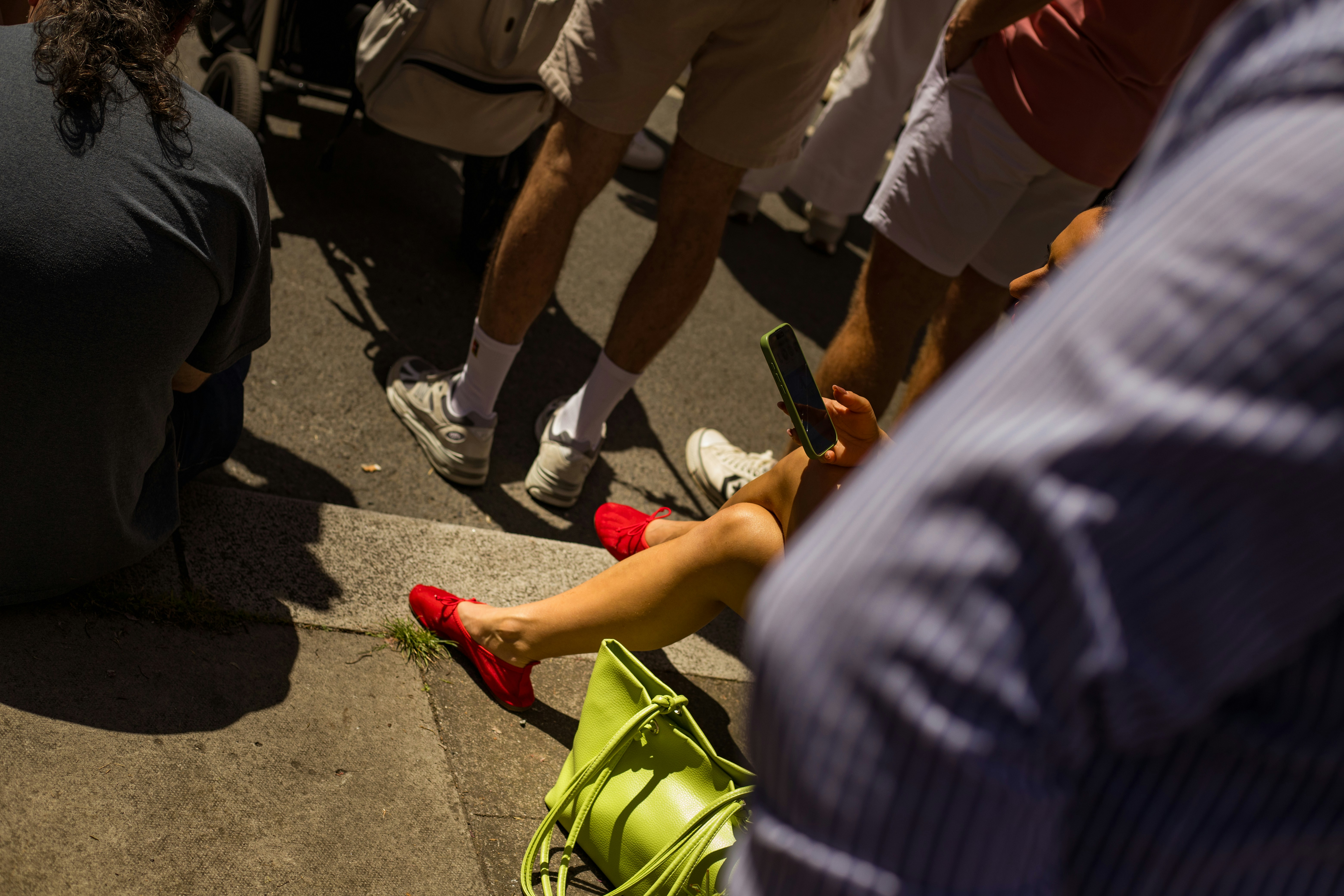 Femme en chaussures rouges assise par terre avec un sac vert.