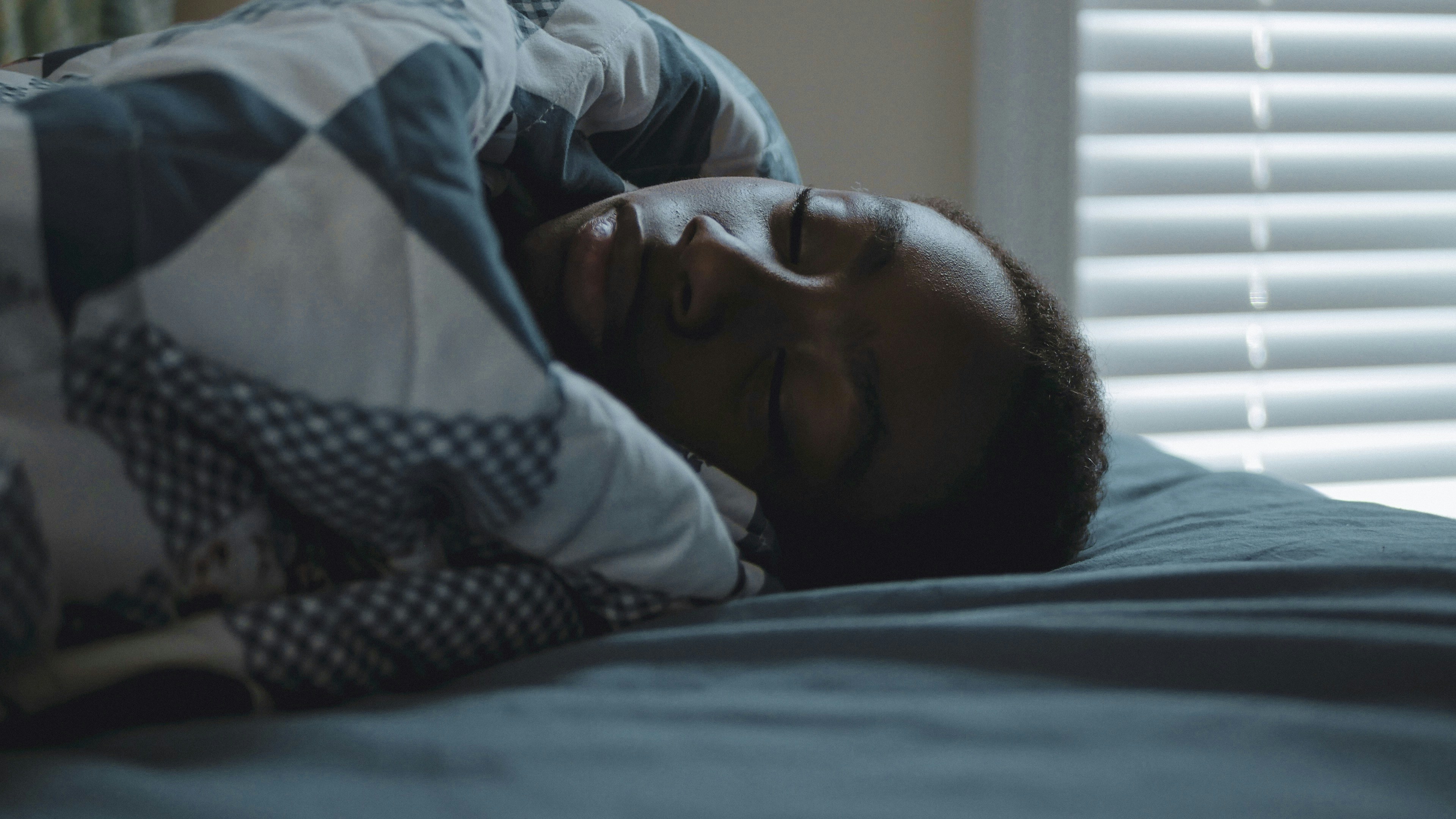 A person sleeping peacefully in bed under a patterned blanket.