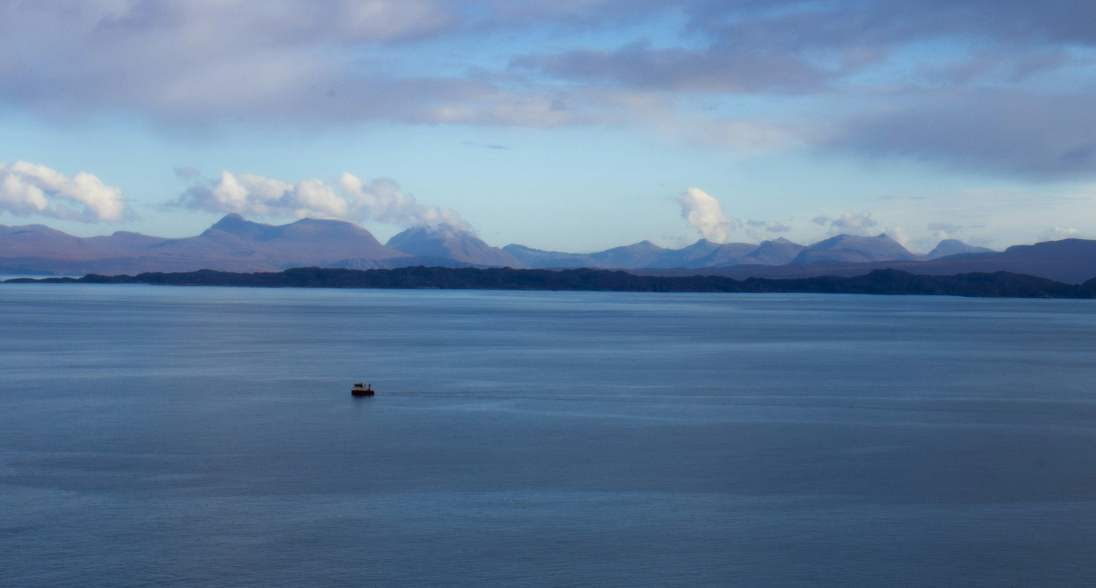 Distant mountains and a small boat on calm blue water.