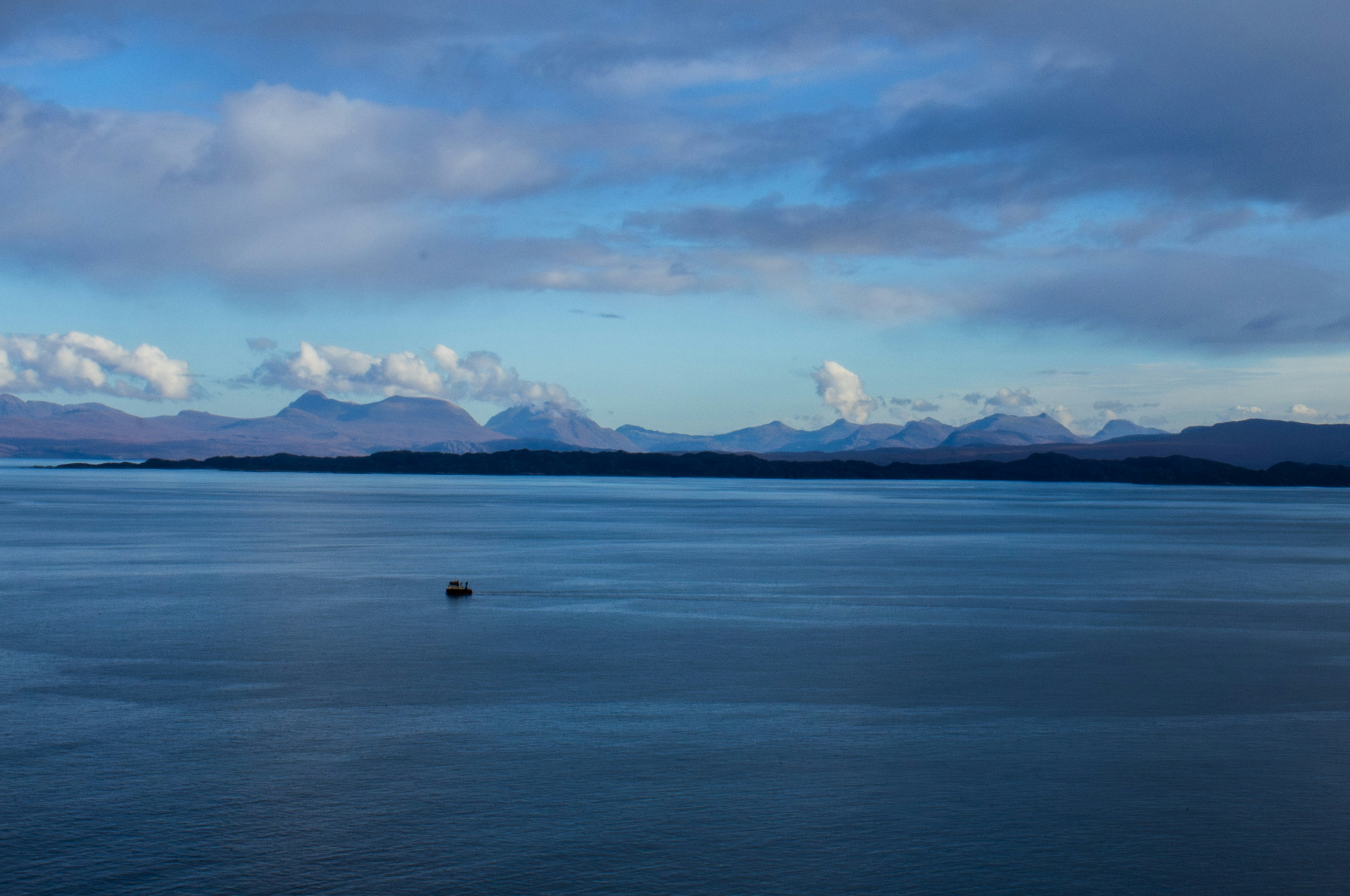 Serene blue water, distant mountains, and a cloudy sky.