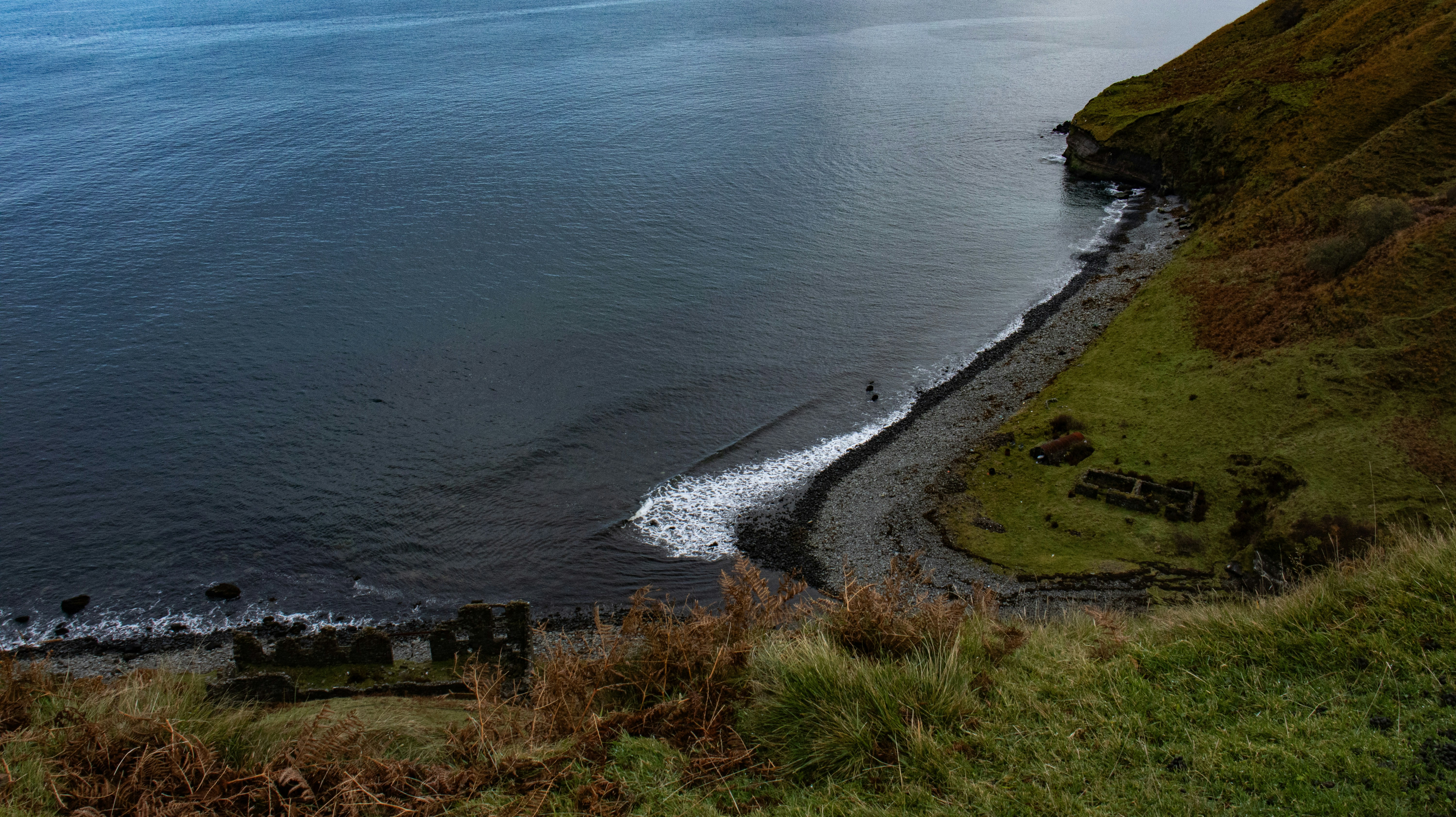 Rugged coastline with dark ocean, pebble beach, and ancient ruins.