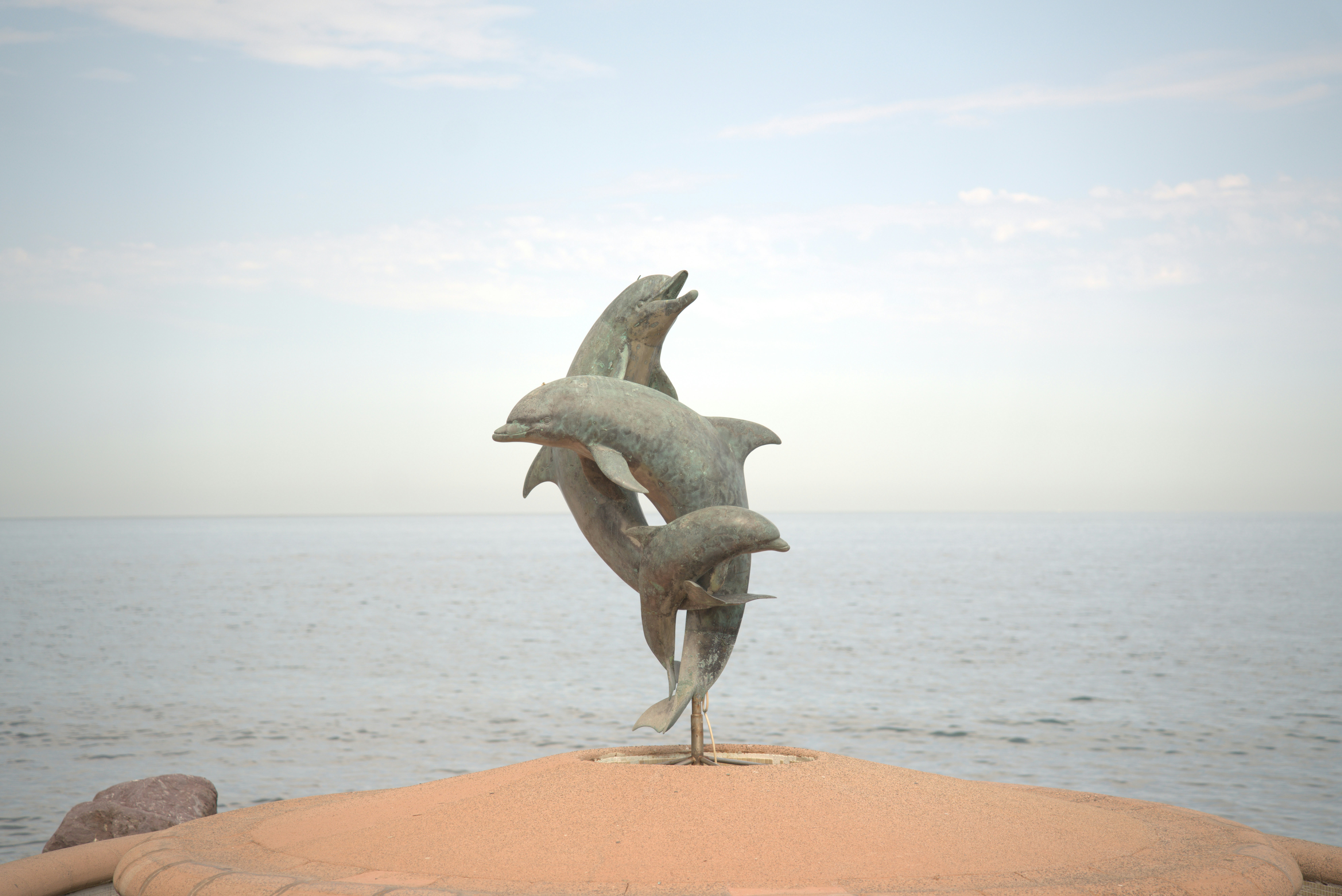Dolphin sculpture by the ocean under a cloudy sky