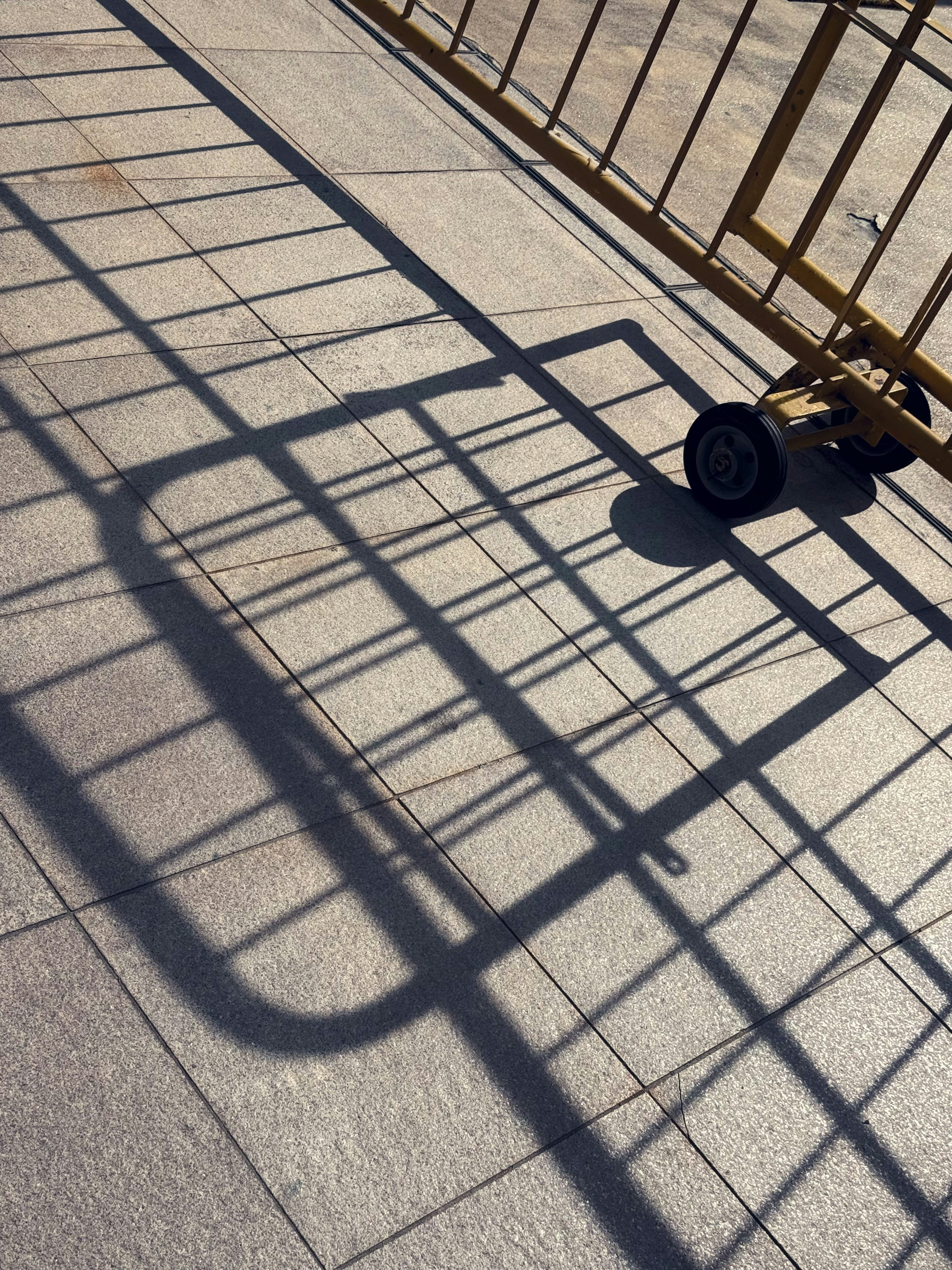 Long shadows of a metal barrier on a tiled ground.