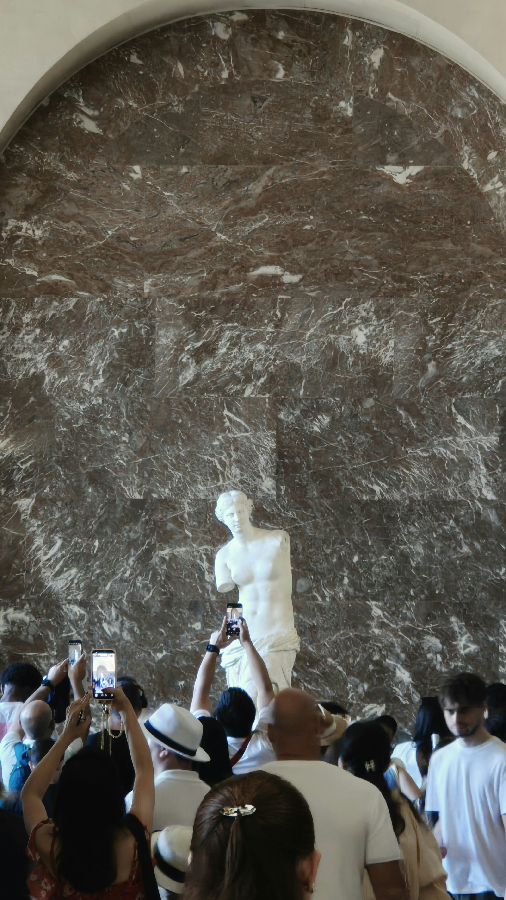 People photographing a marble statue in a museum.