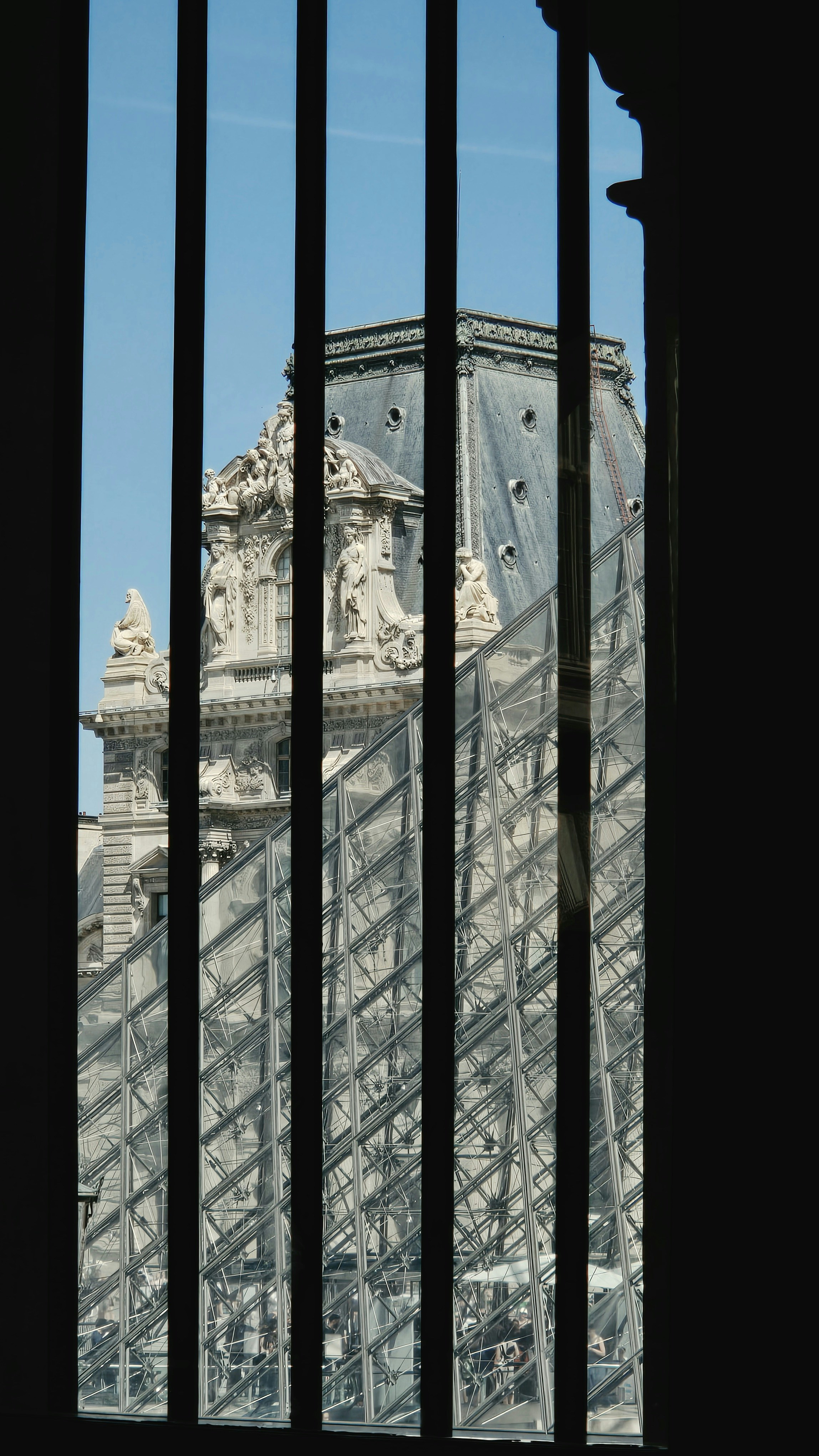 Louvre pyramid and classical building viewed through dark bars.