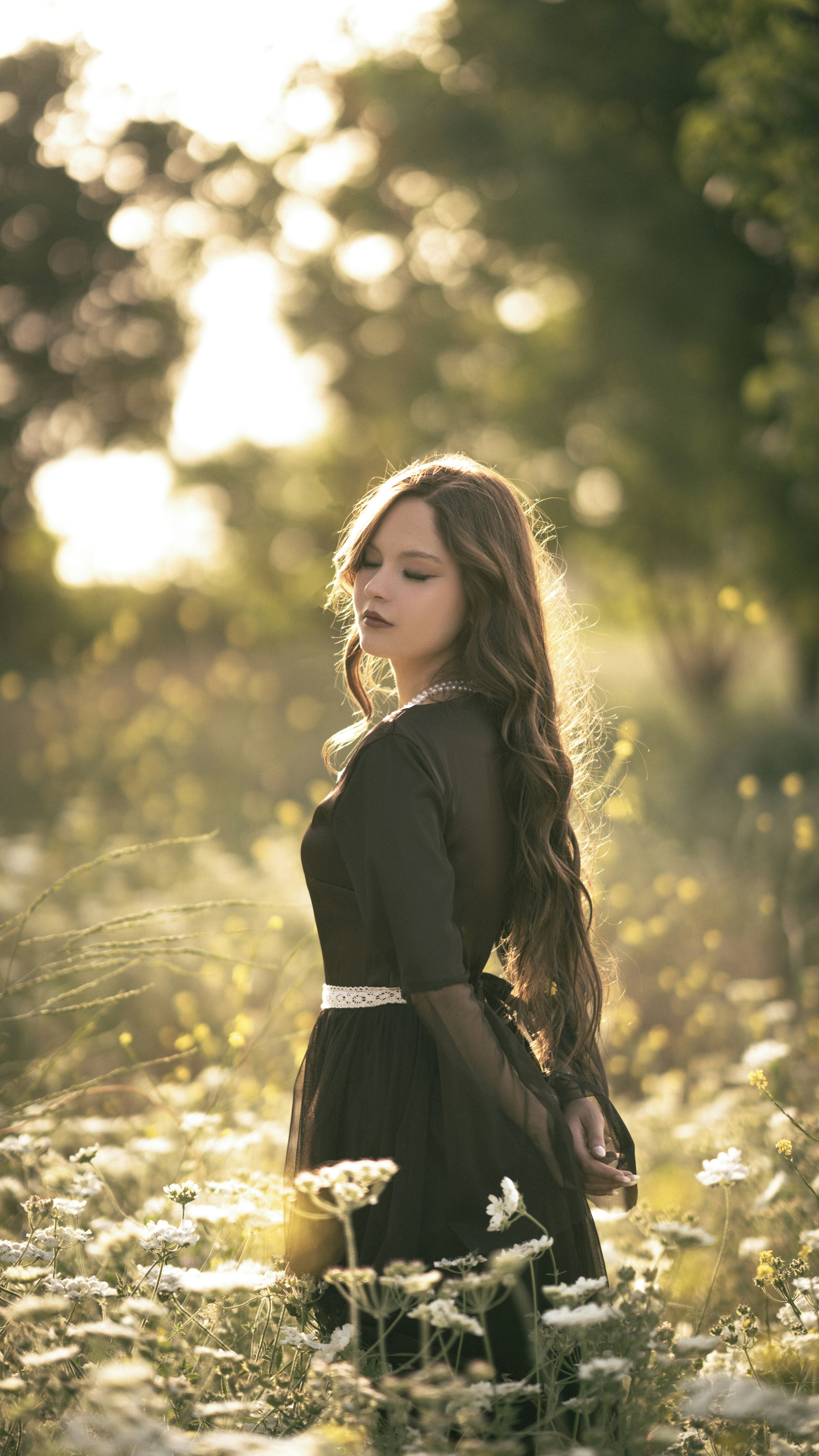 Woman in dark dress standing in sunlit field of wildflowers