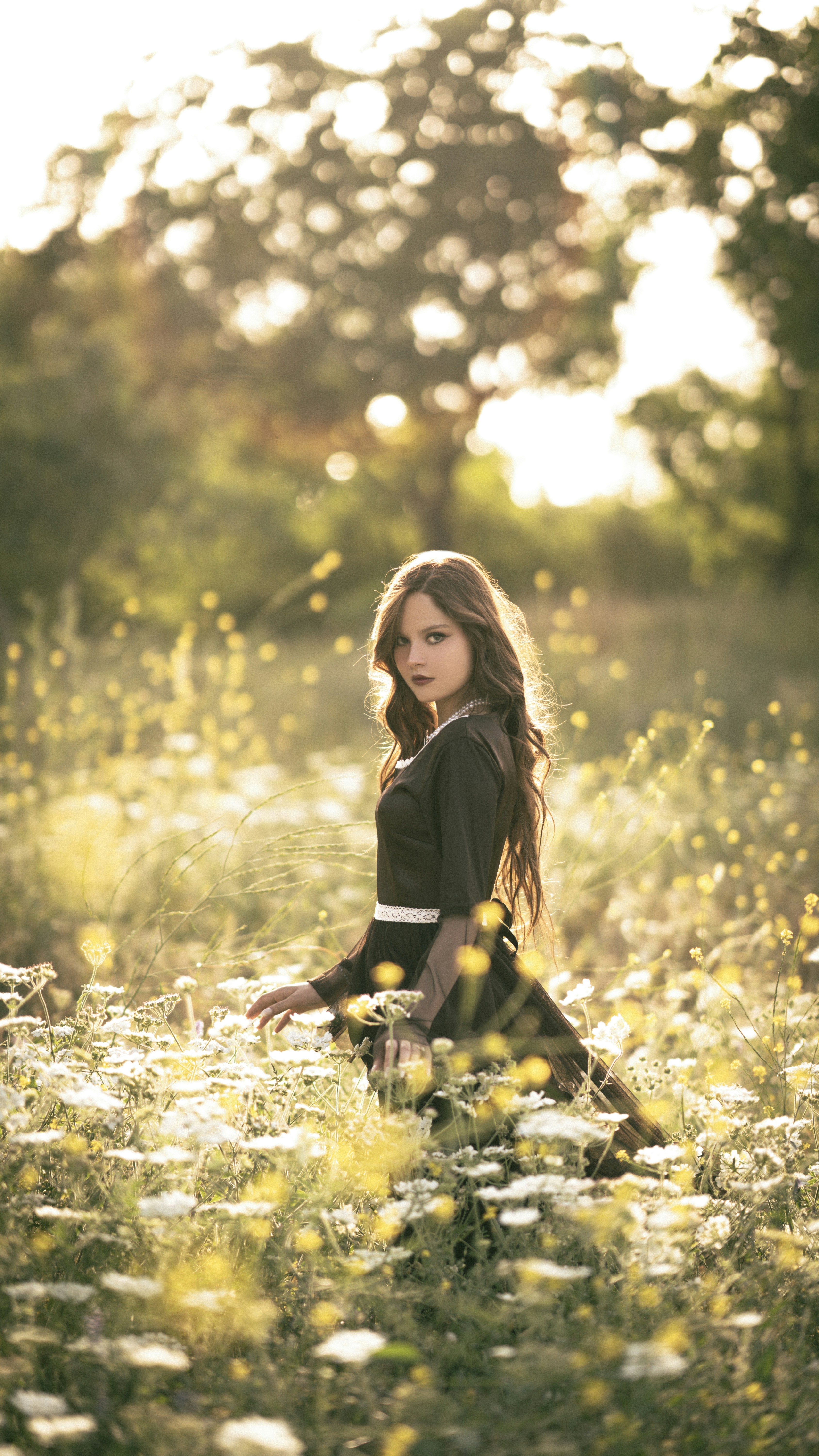 A young girl sits among wildflowers bathed in golden light