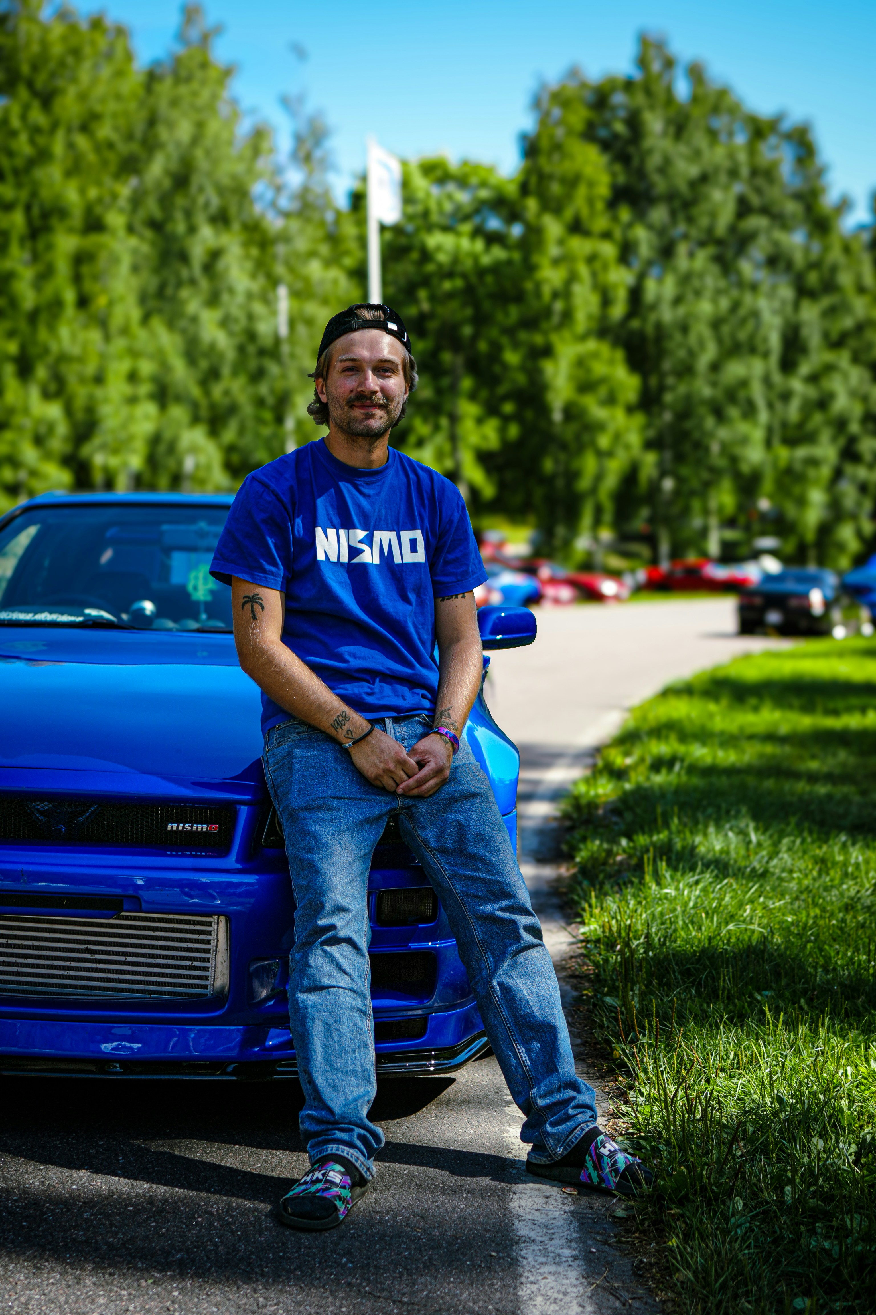 Un homme portant un t-shirt bleu Nismo se tient près d’une voiture bleue