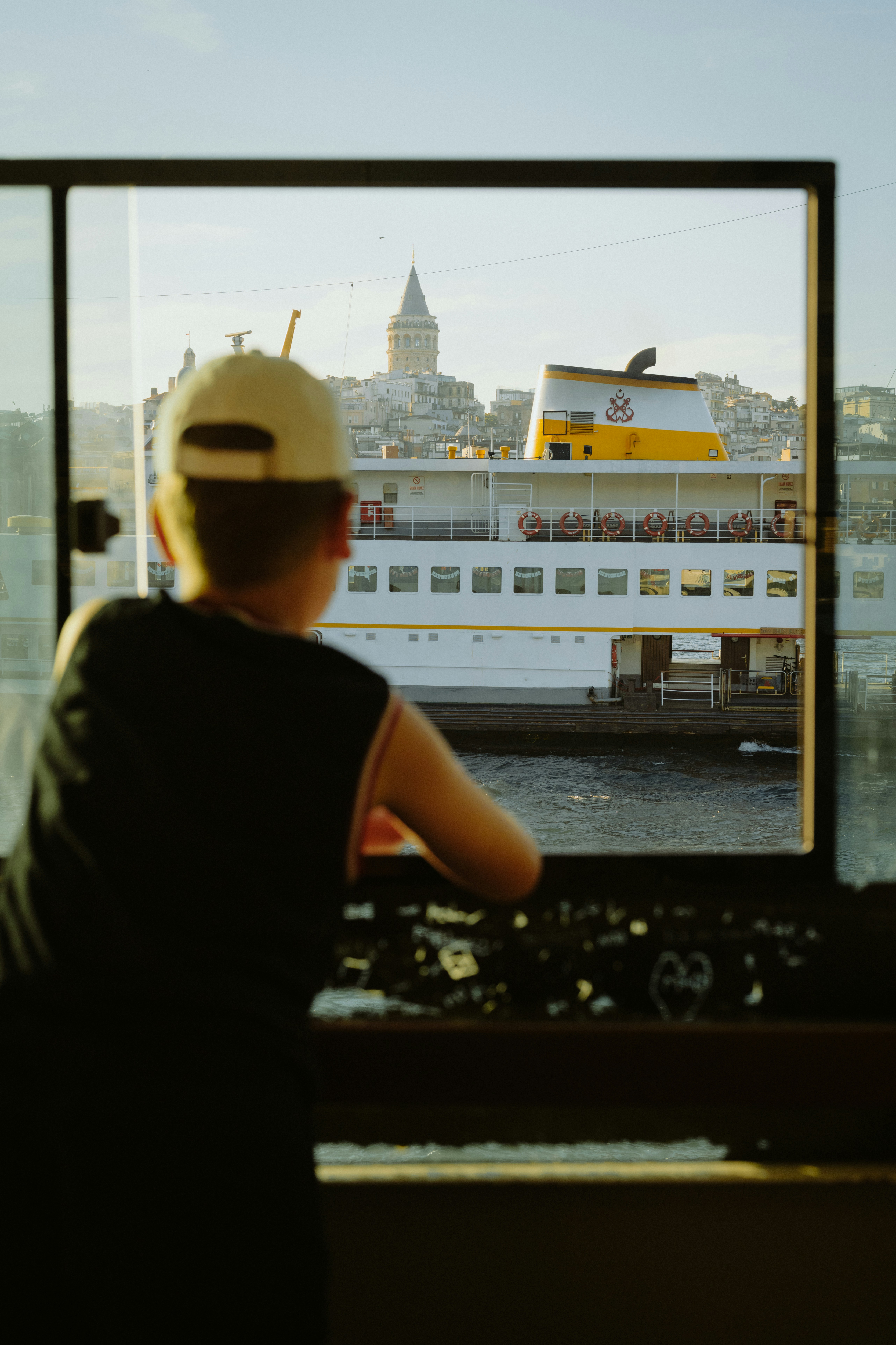 Boy looks out window at ferry and galata tower.