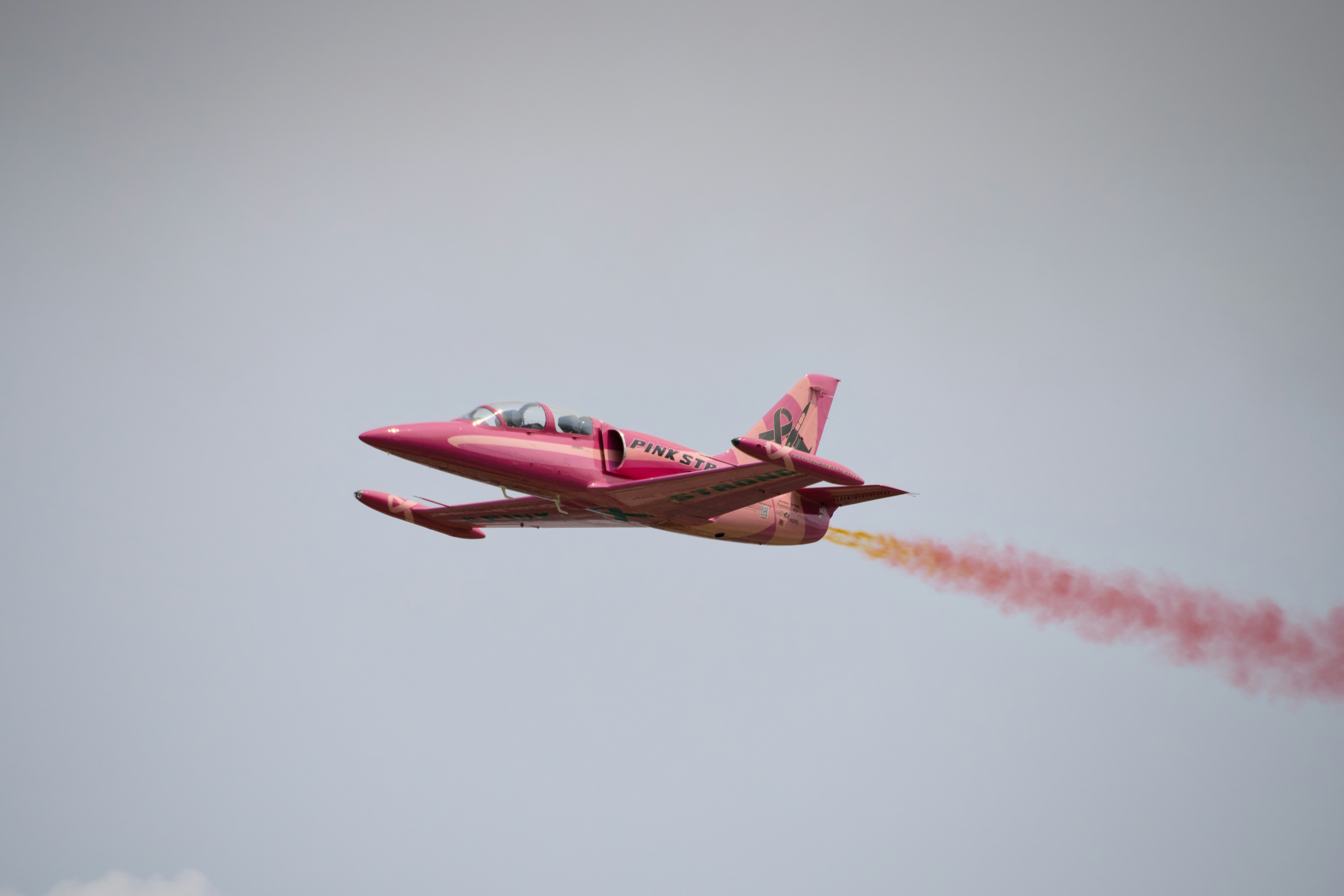 Pink jet aircraft flying with a vibrant red smoke trail