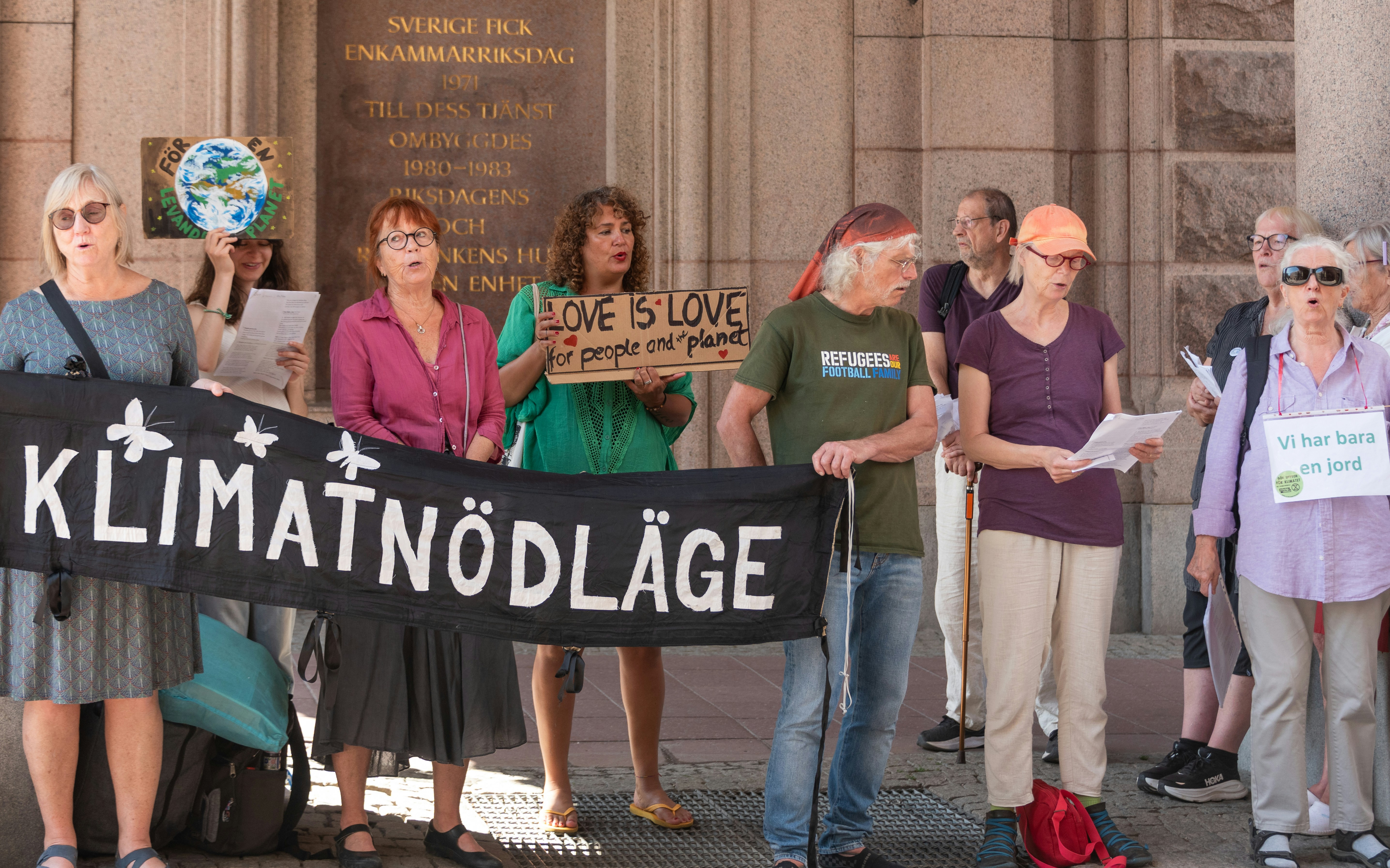 Demonstrators hold "klimatnödläge" banner and signs for climate and love.