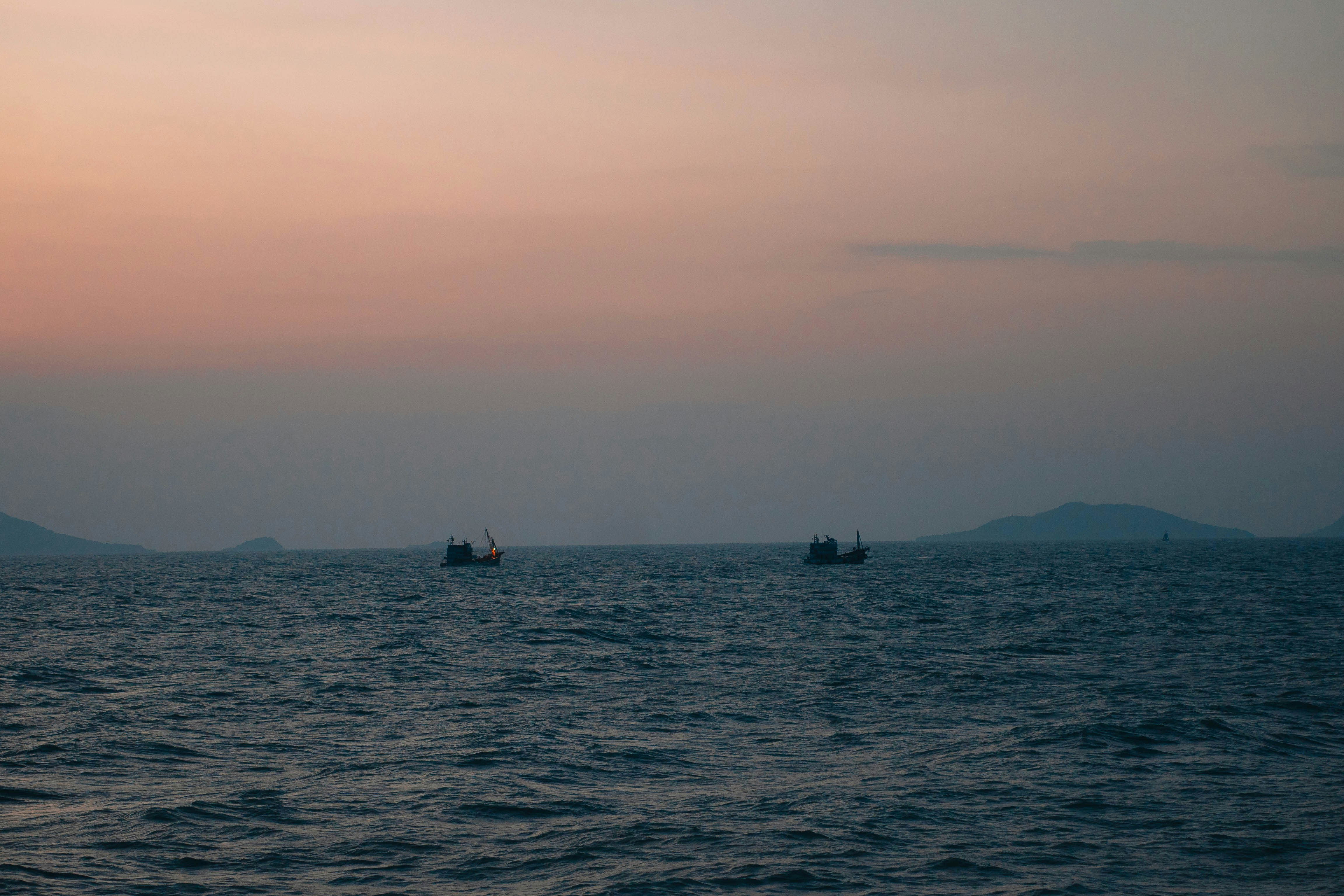 Two boats on the ocean at sunset with distant land