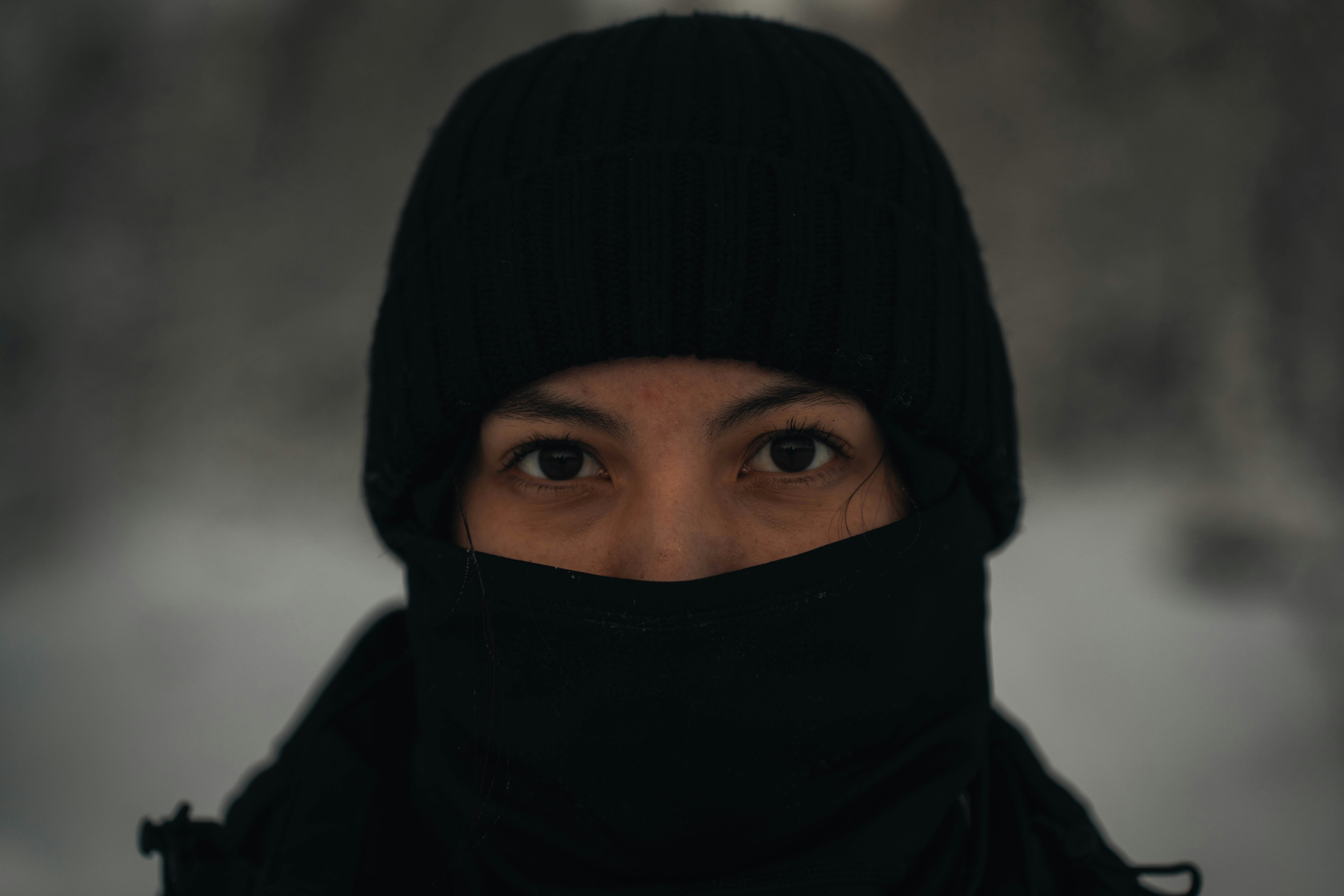 A person's eyes are visible in a black balaclava