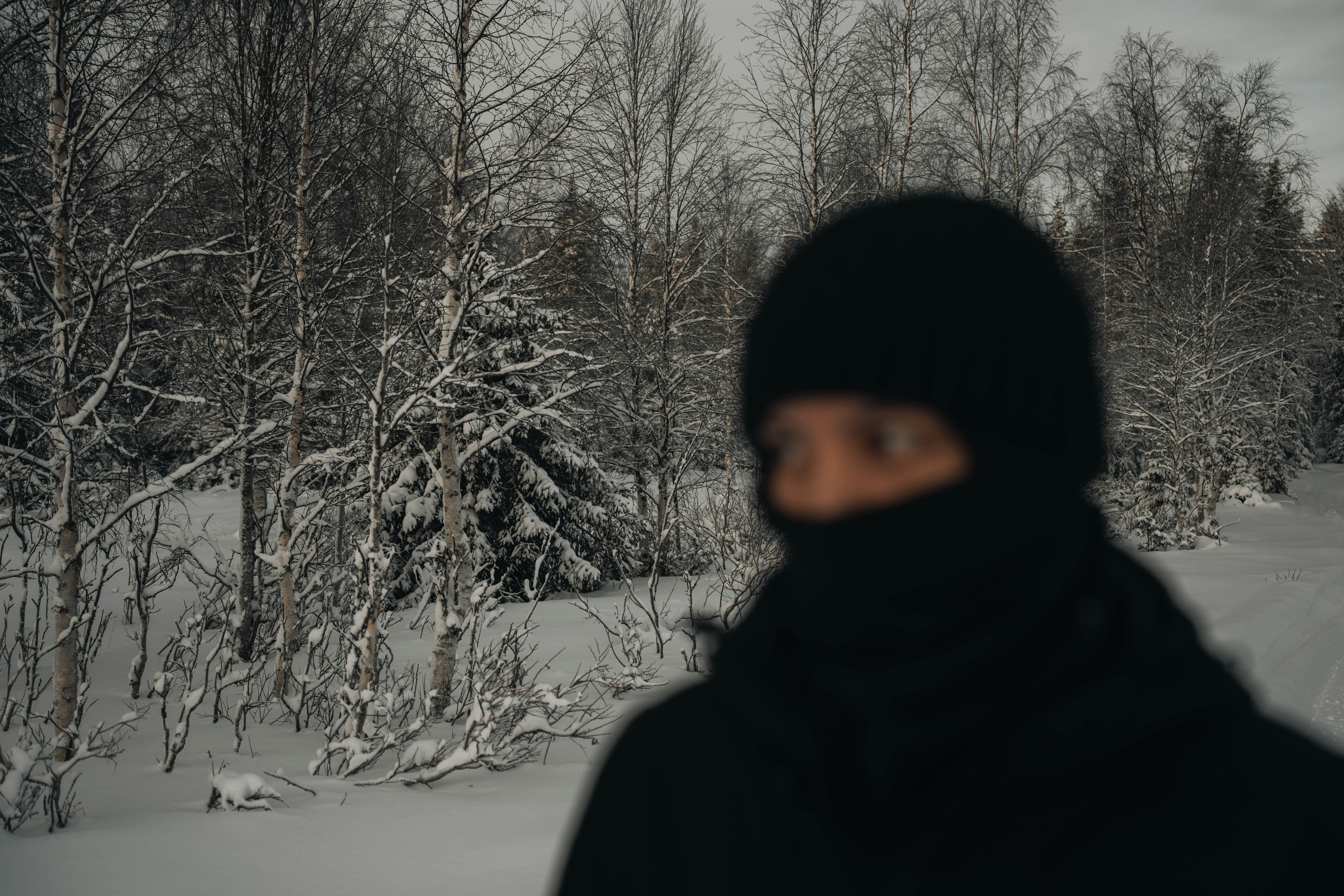 雪の冬の森で黒いバラクラバをかぶった人物。