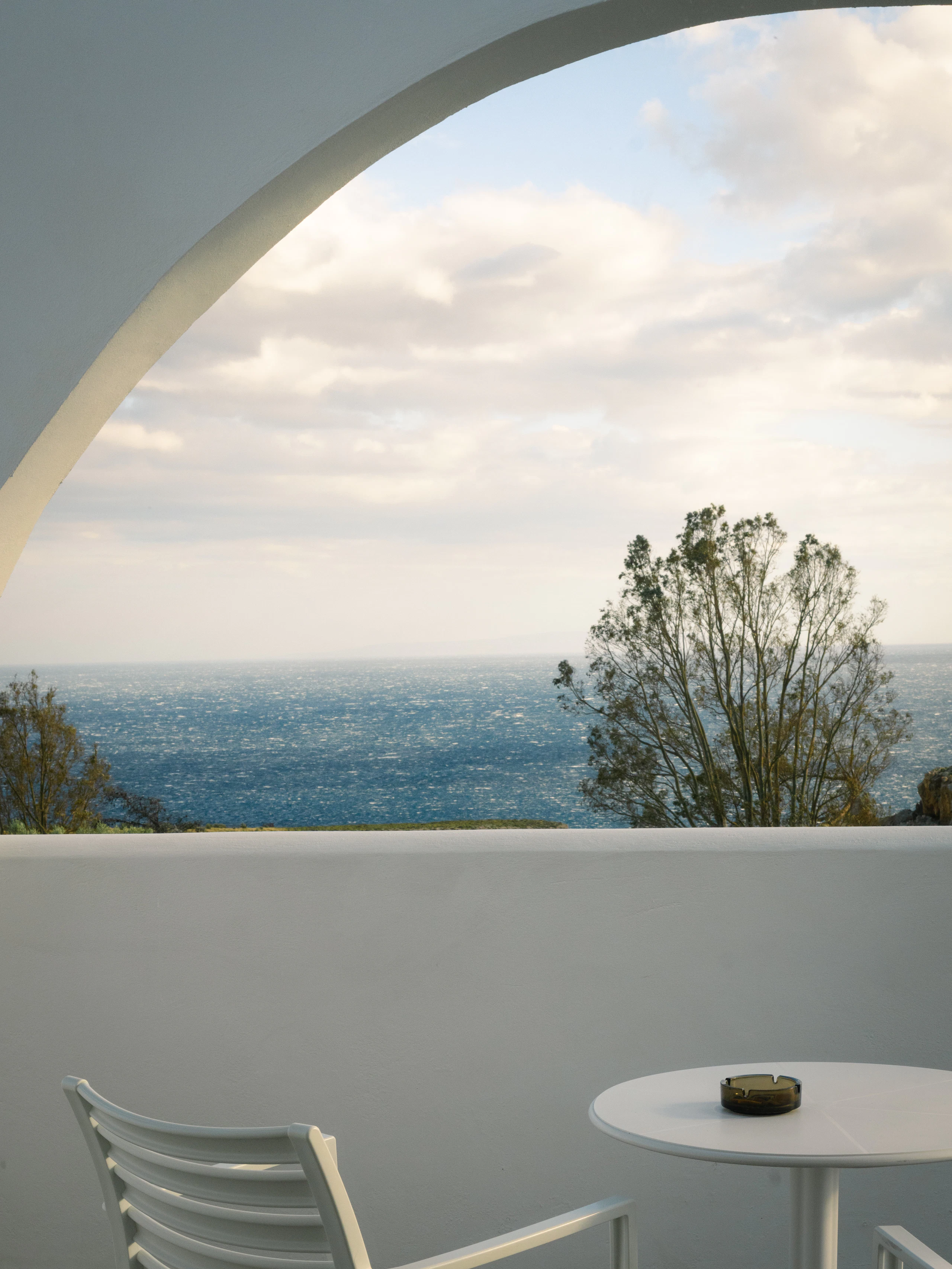 White balcony with a chair and table over a blue ocean