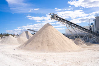 Large sand and gravel piles with industrial conveyors.
