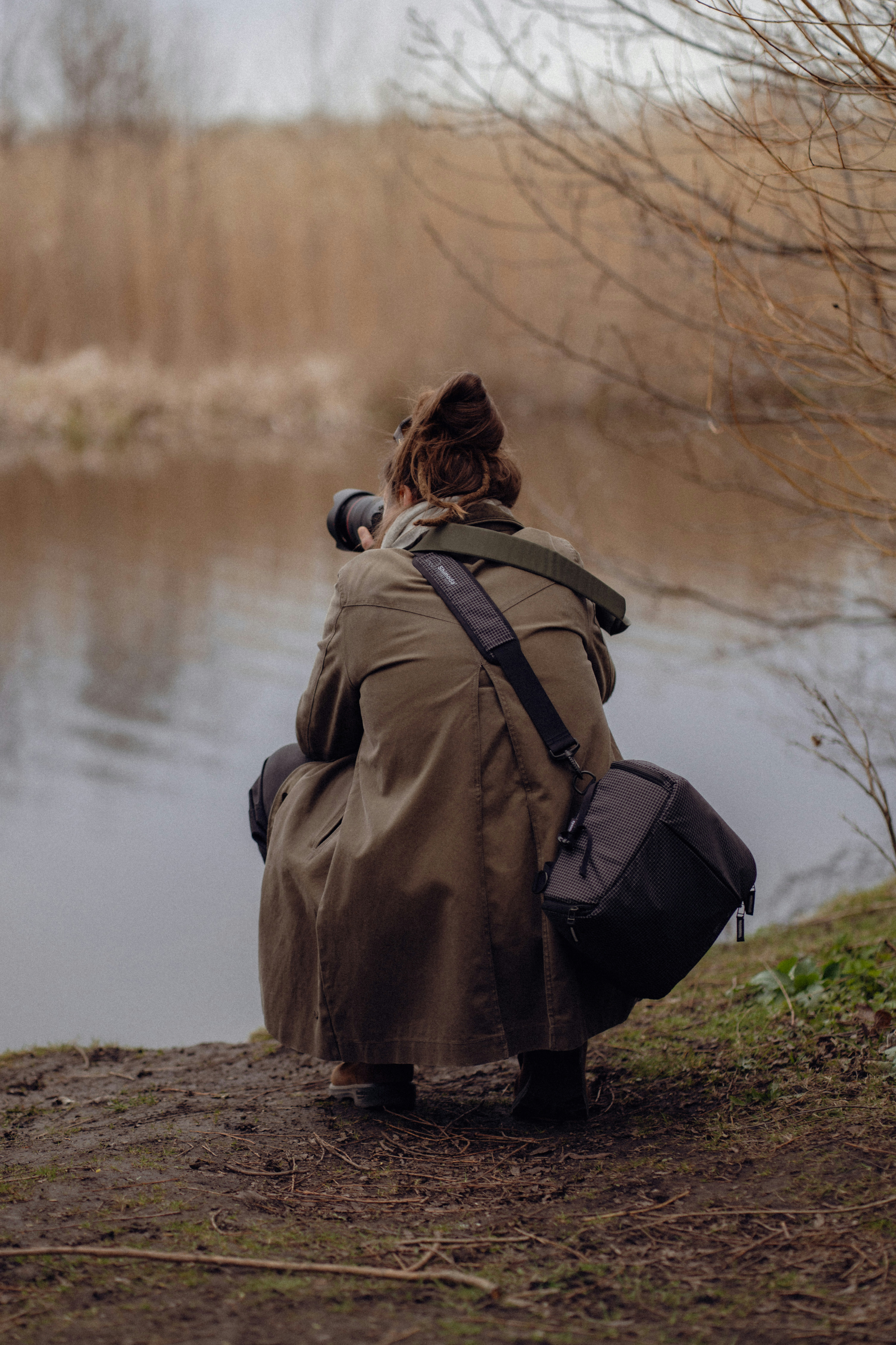 Une personne accroupie près de l’eau, photographiant avec un appareil photo