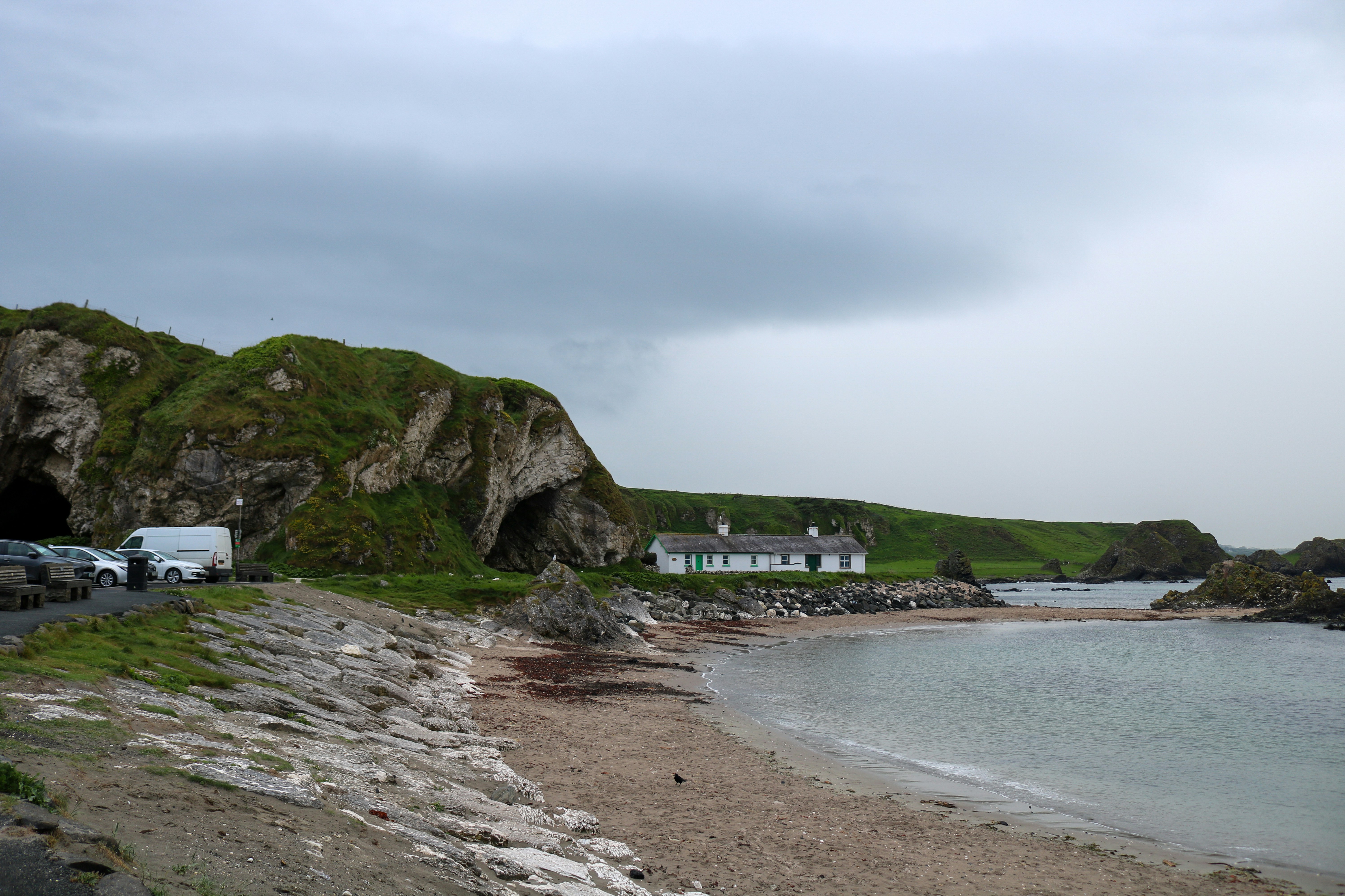 Coastal scene with cliffs, caves, a beach, and a house.