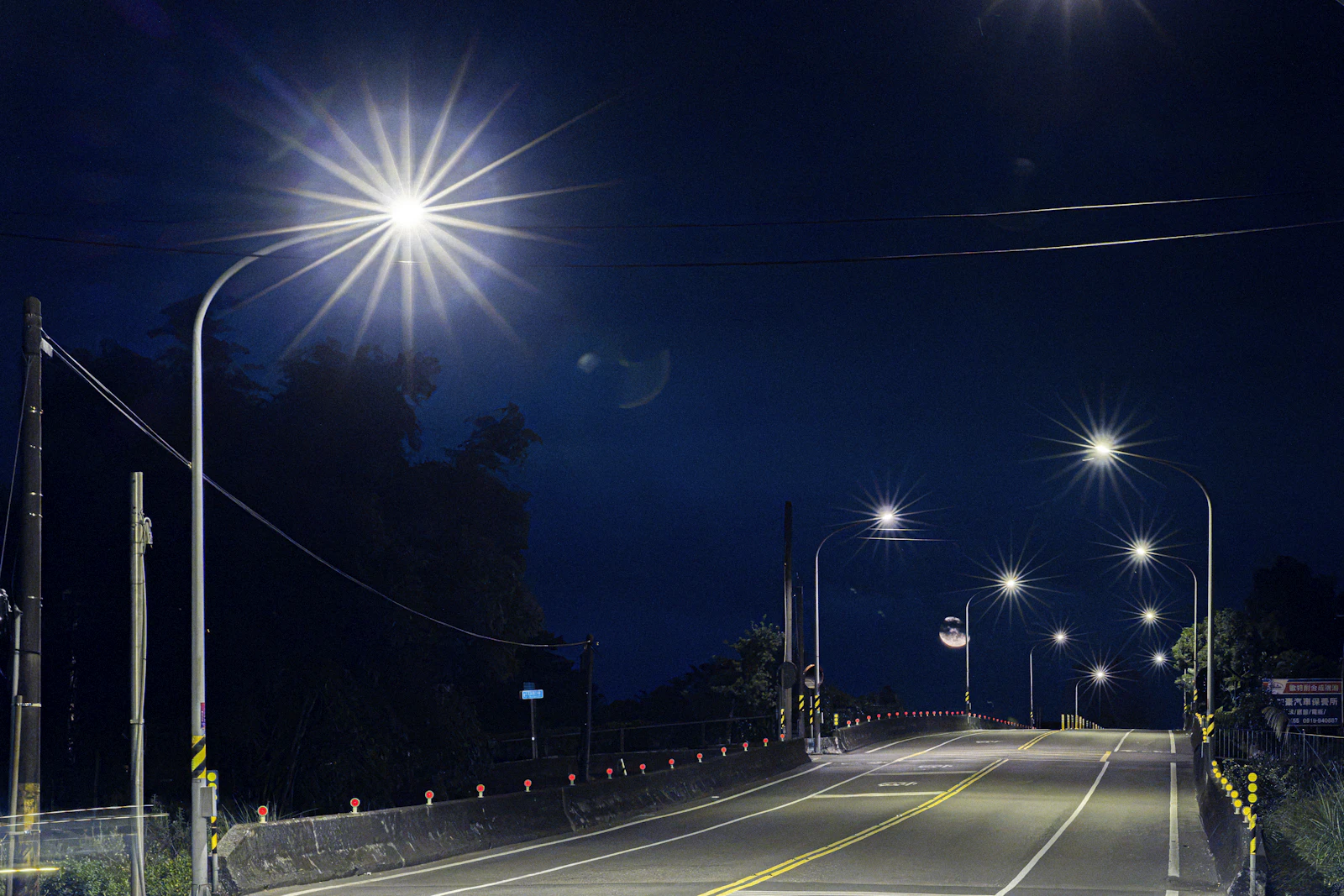 An empty road curving through the dark with distant city lights