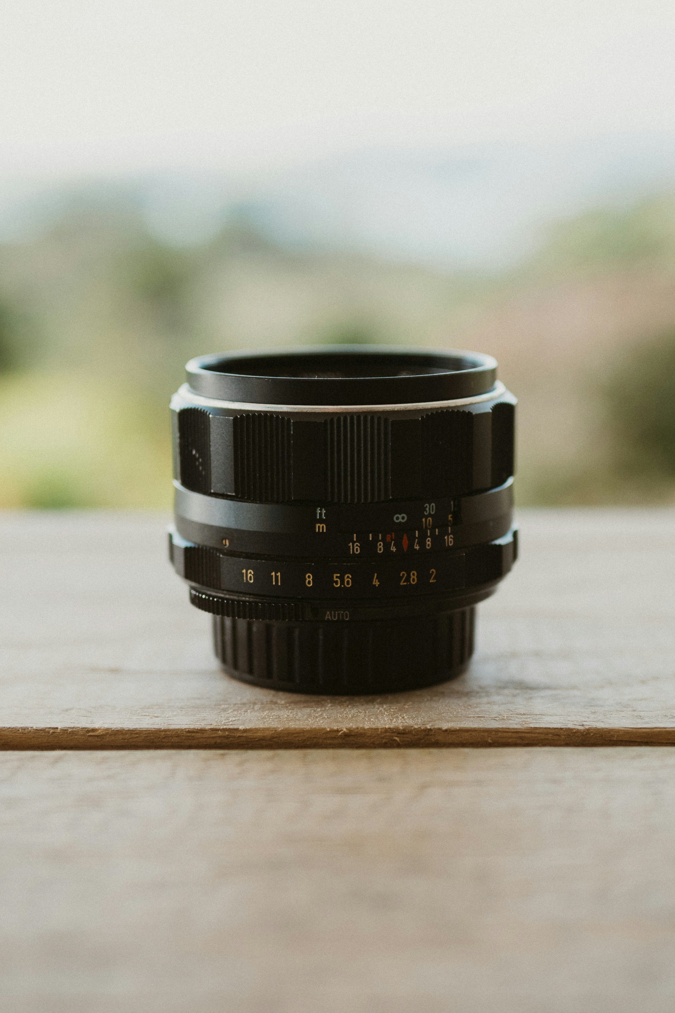 A black camera lens sits on a wooden table