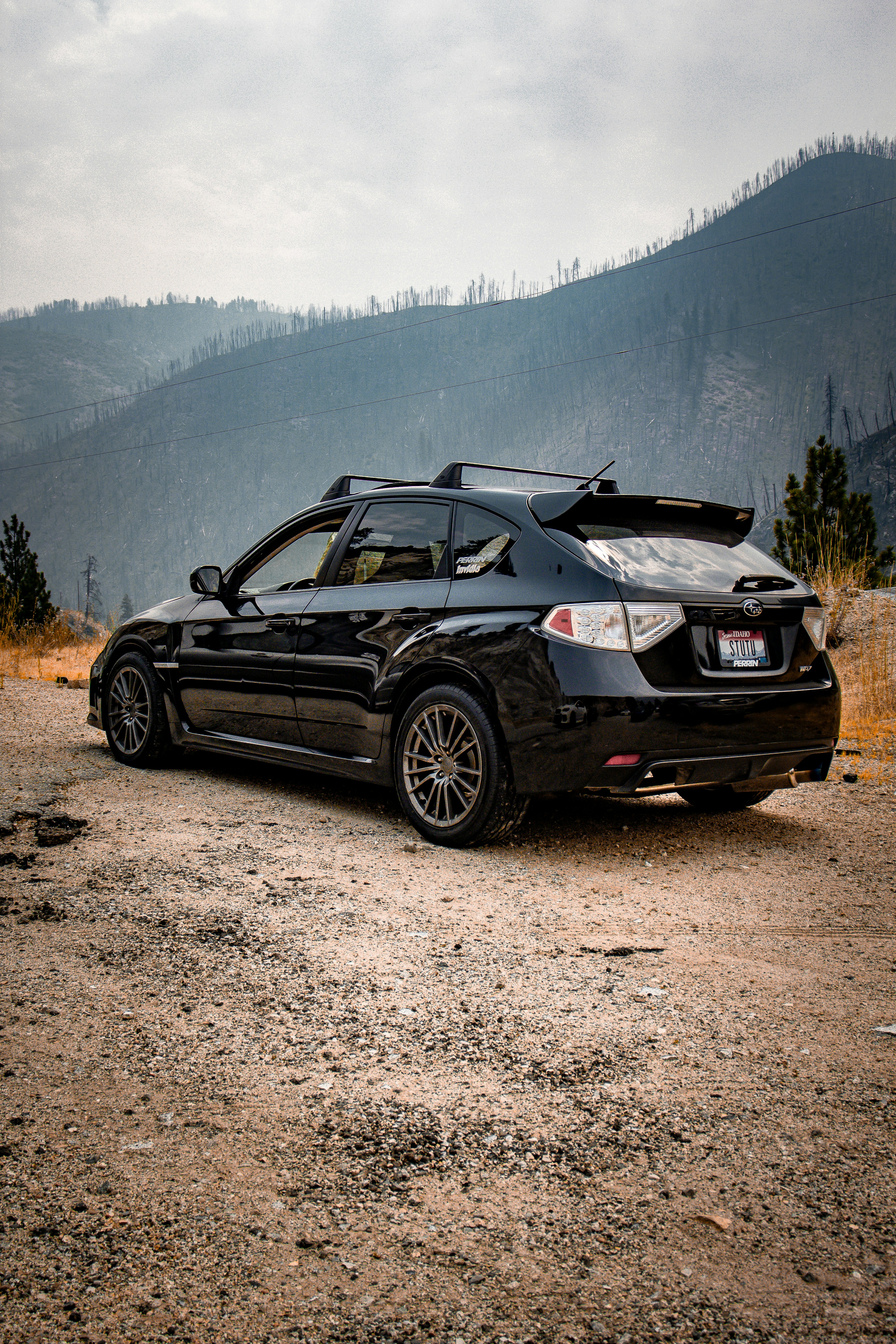 Coche hatchback negro en un camino de tierra con fondo de montaña y brumoso.