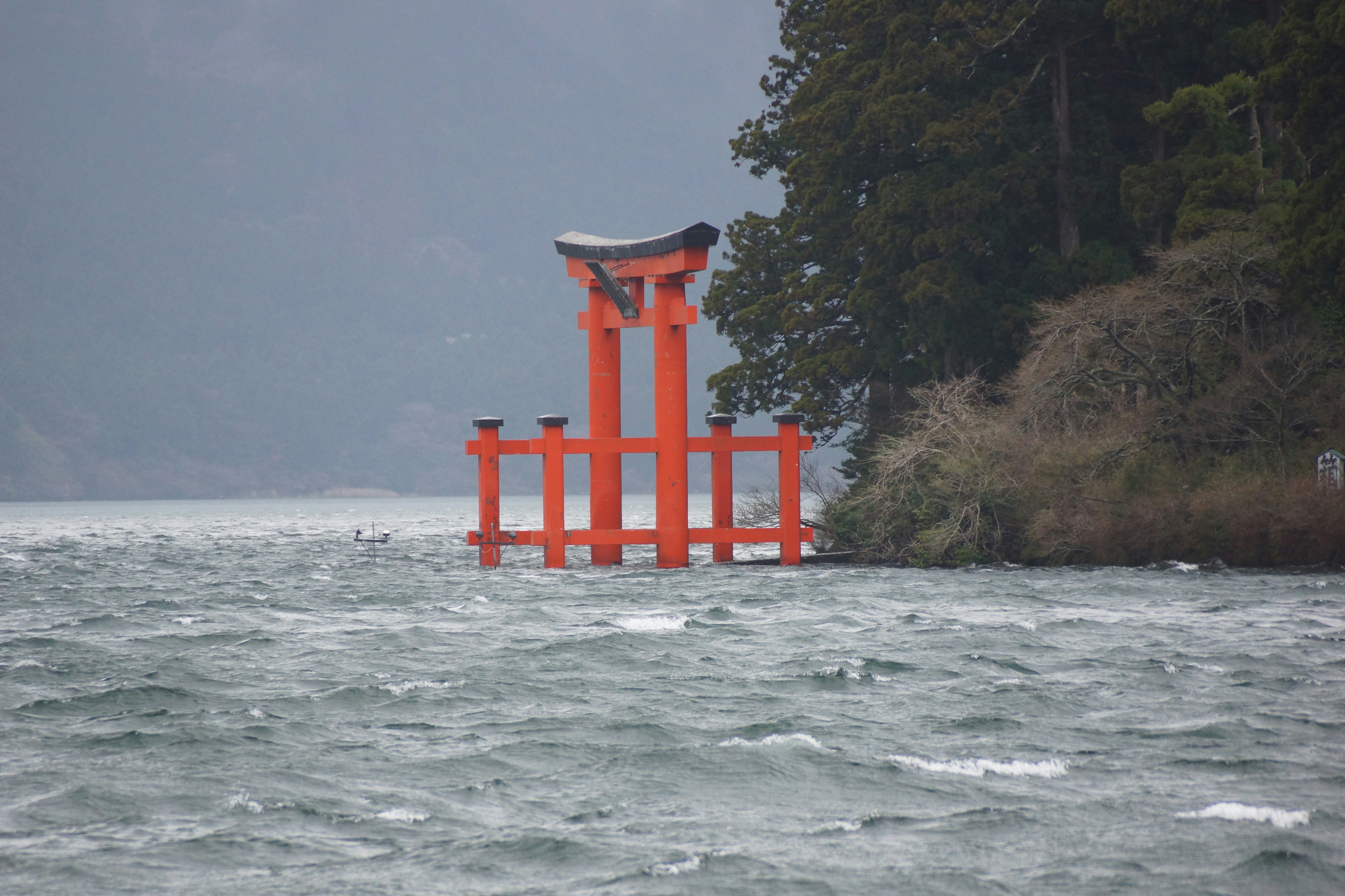 Red torii gate submerged in a choppy lake.