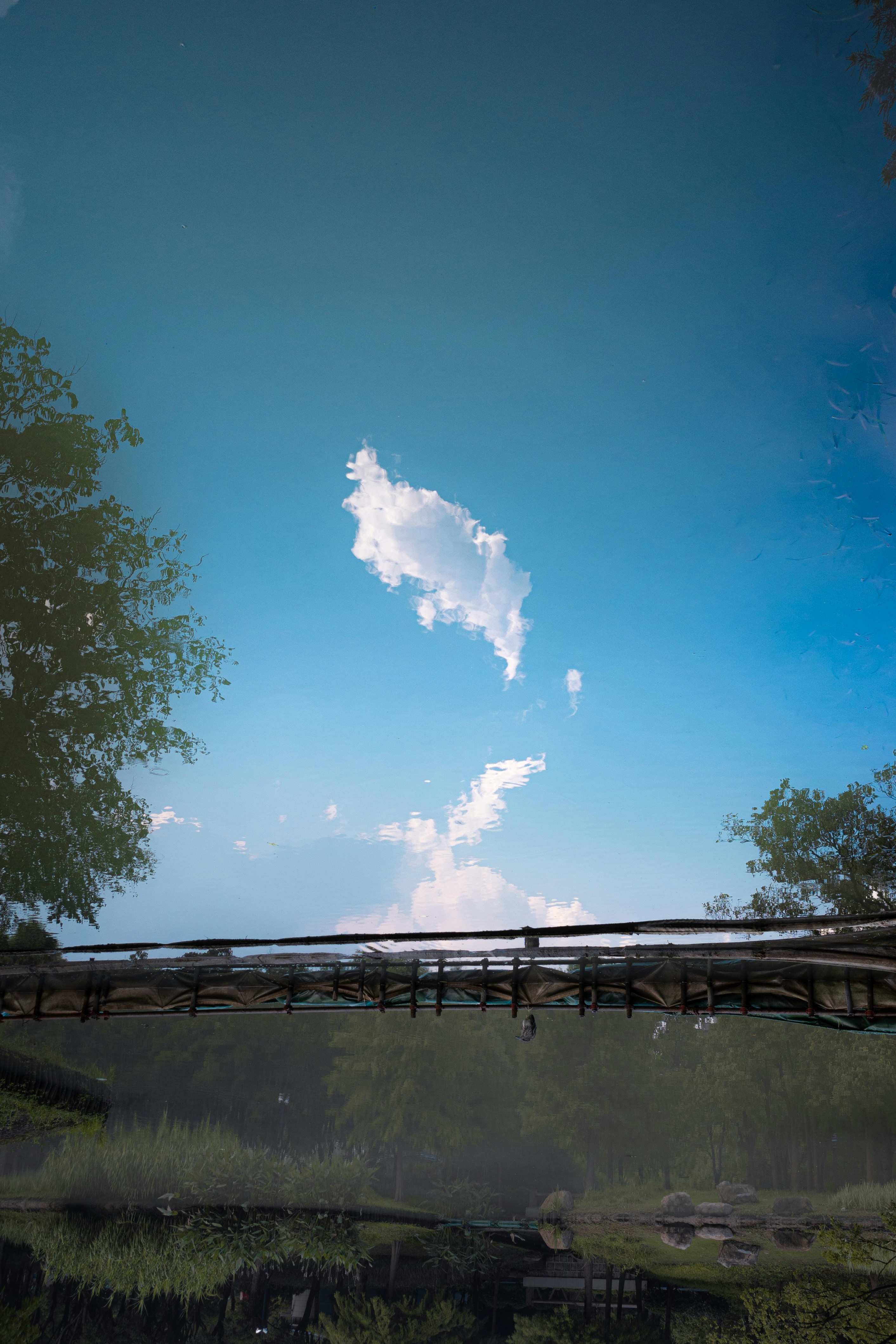 Blue sky and clouds reflected in water with a bridge