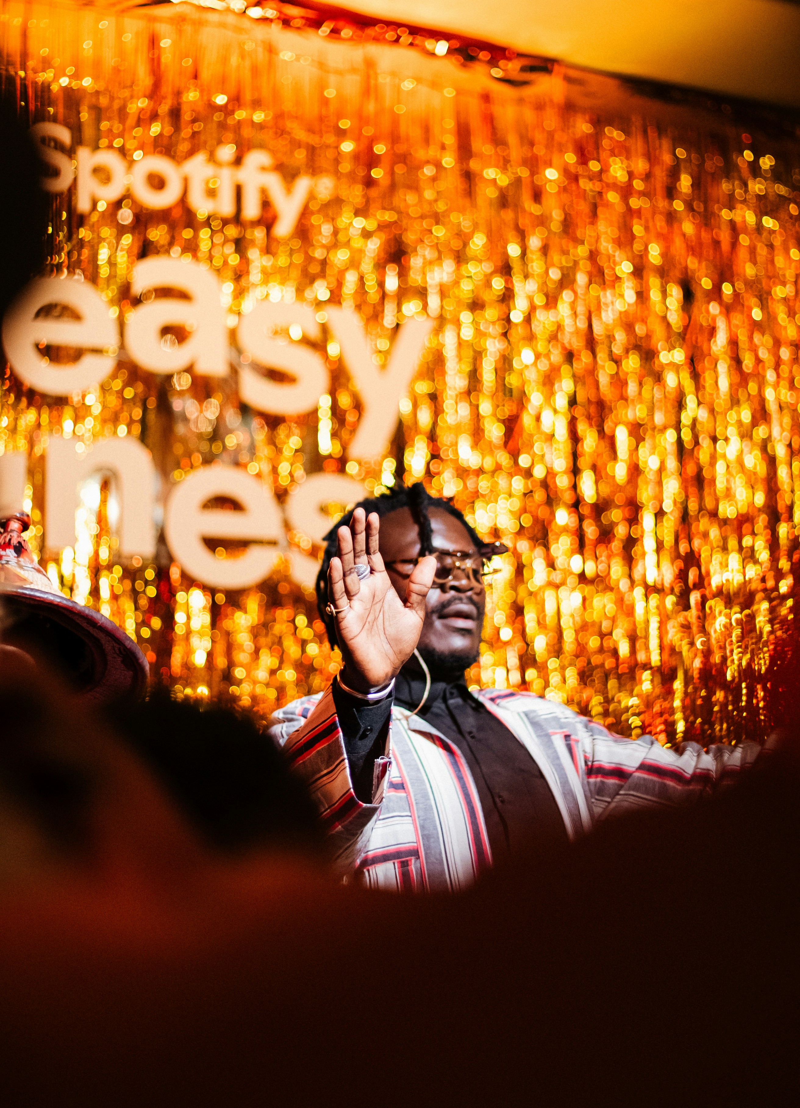 Man on stage with raised hand against golden spotify backdrop.
