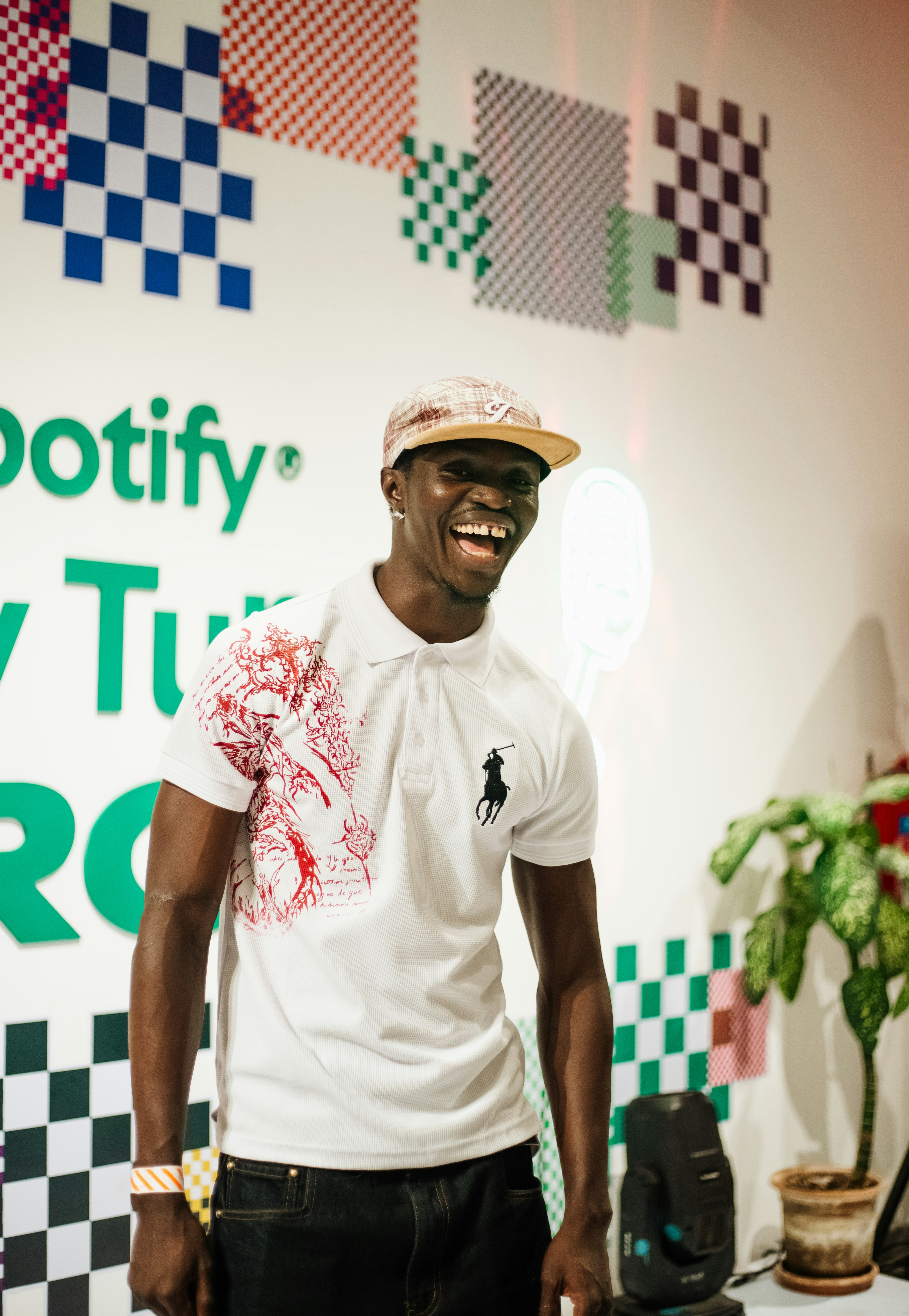 A young man laughing in front of a spotify wall.