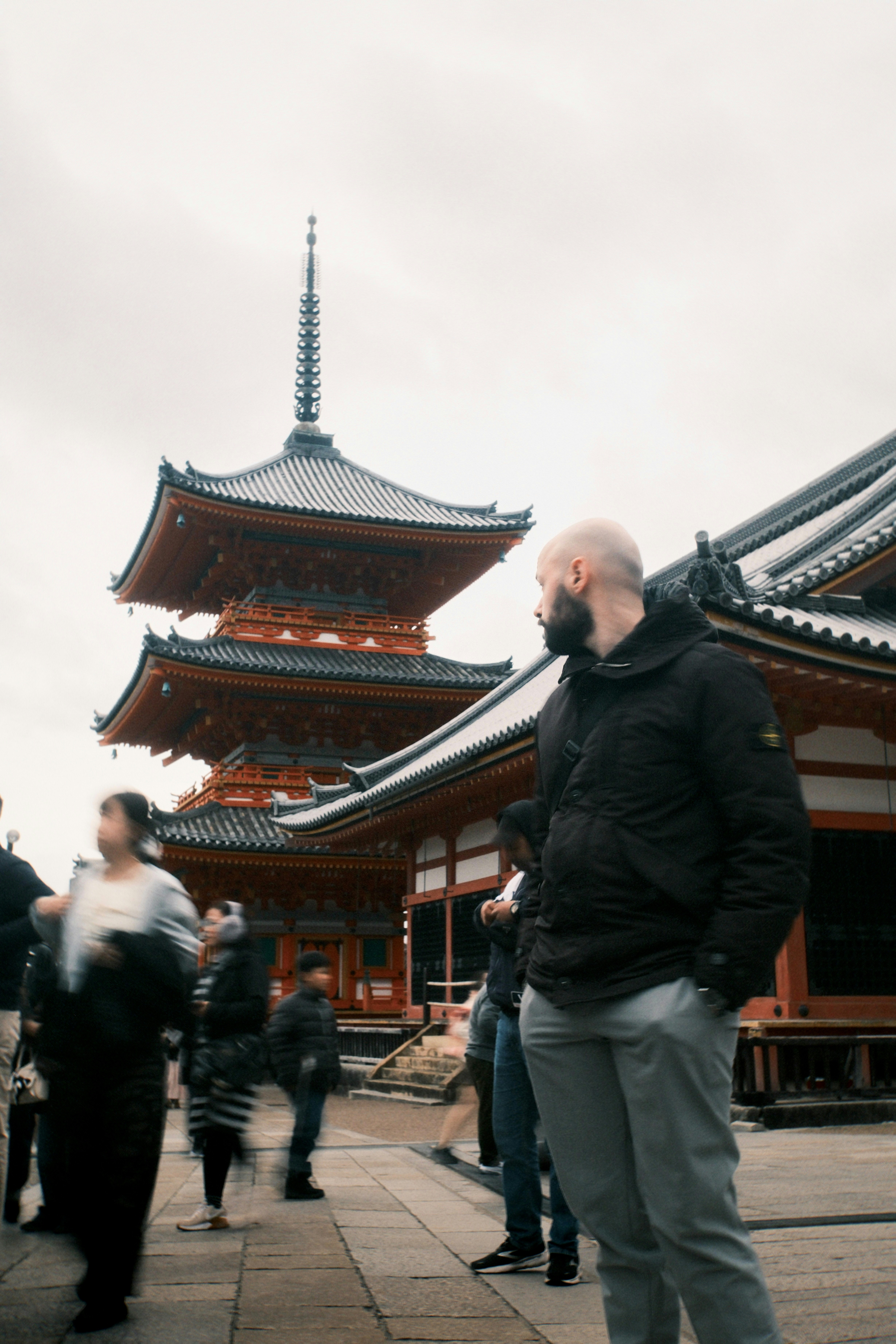 Man in black jacket stands before a vibrant red pagoda