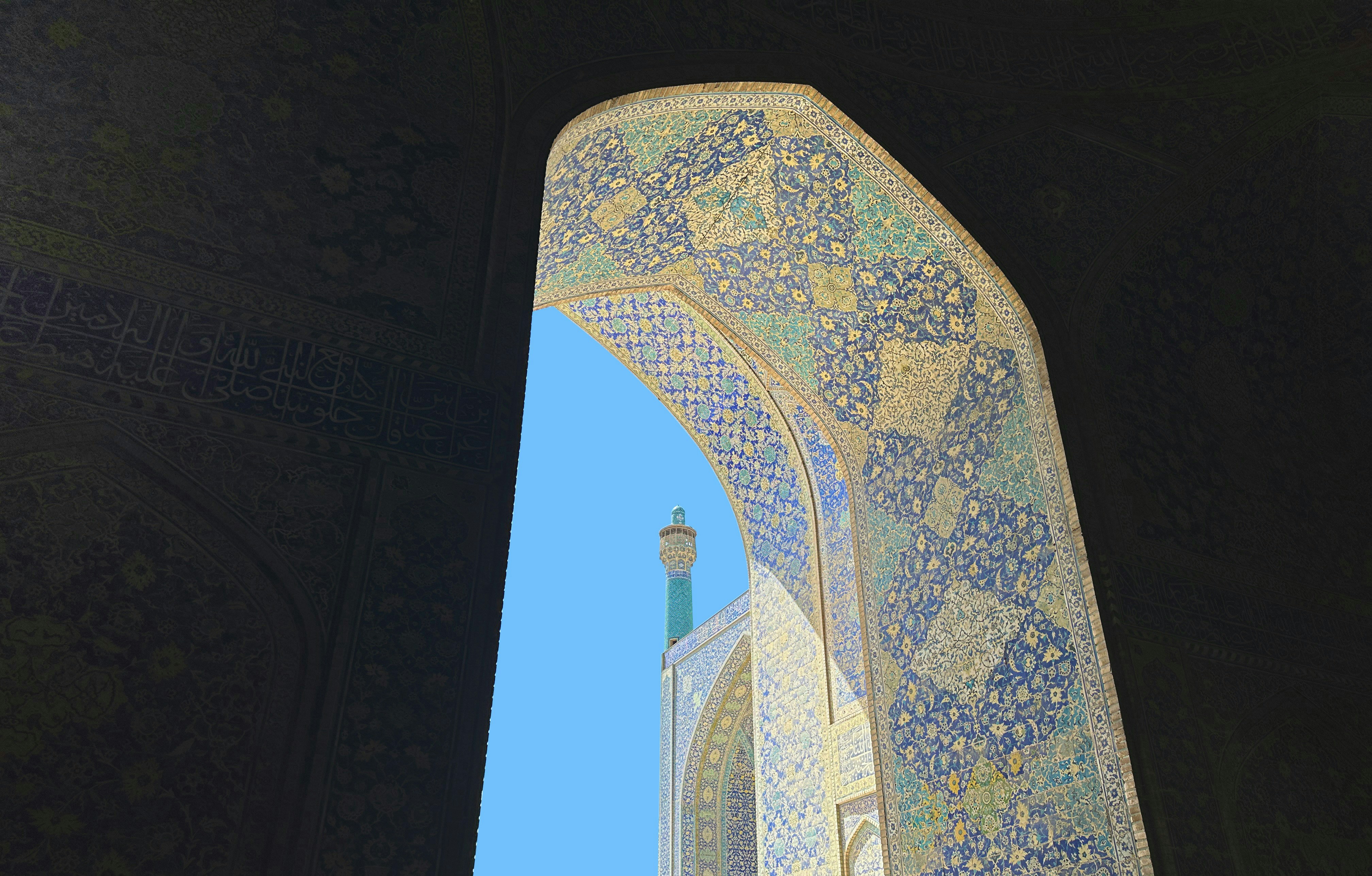 Ornate mosaic archway framing a minaret against a blue sky.
