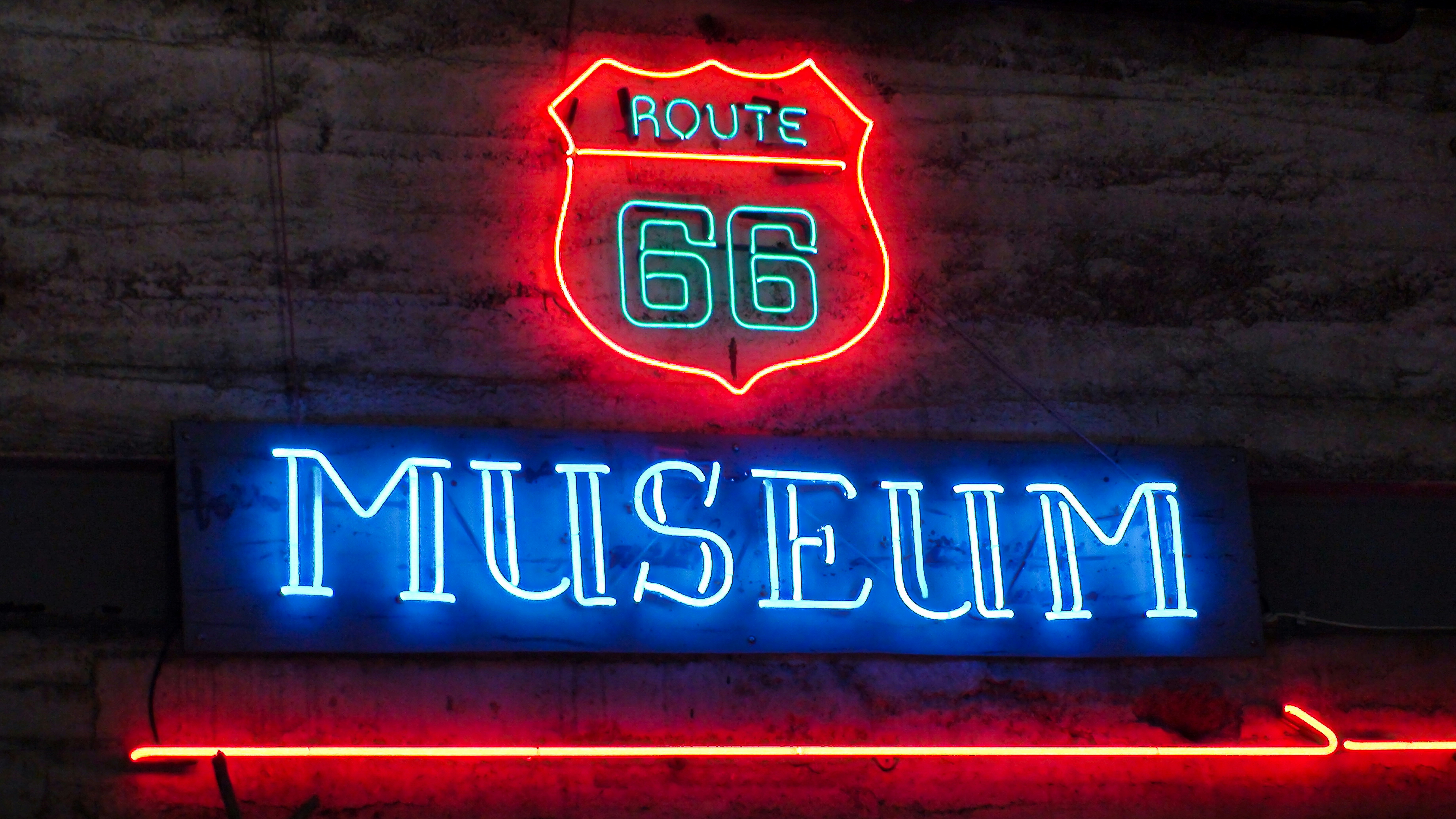 Neon route 66 museum sign glowing brightly on a wall.