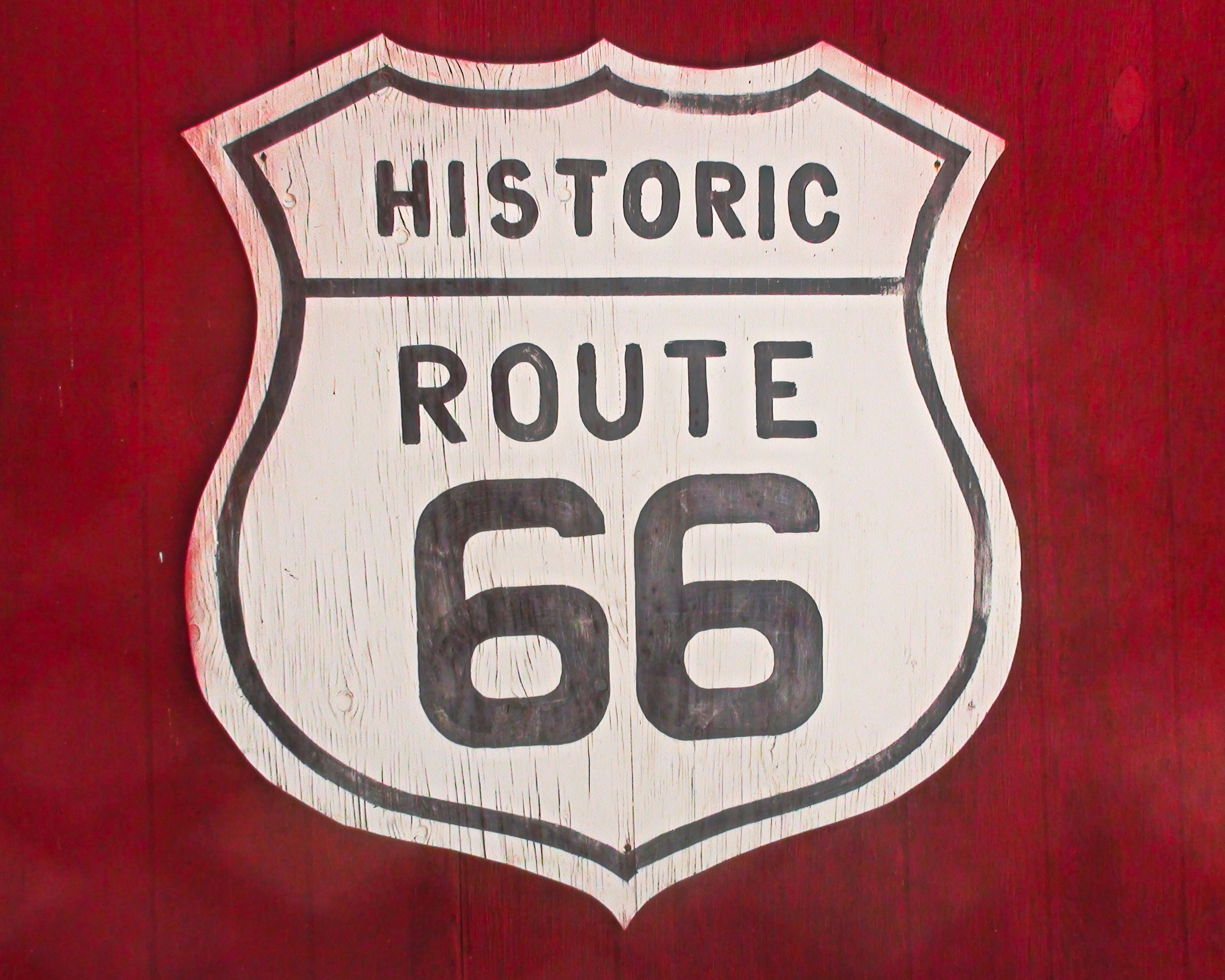 A white historic route 66 sign on a red background.