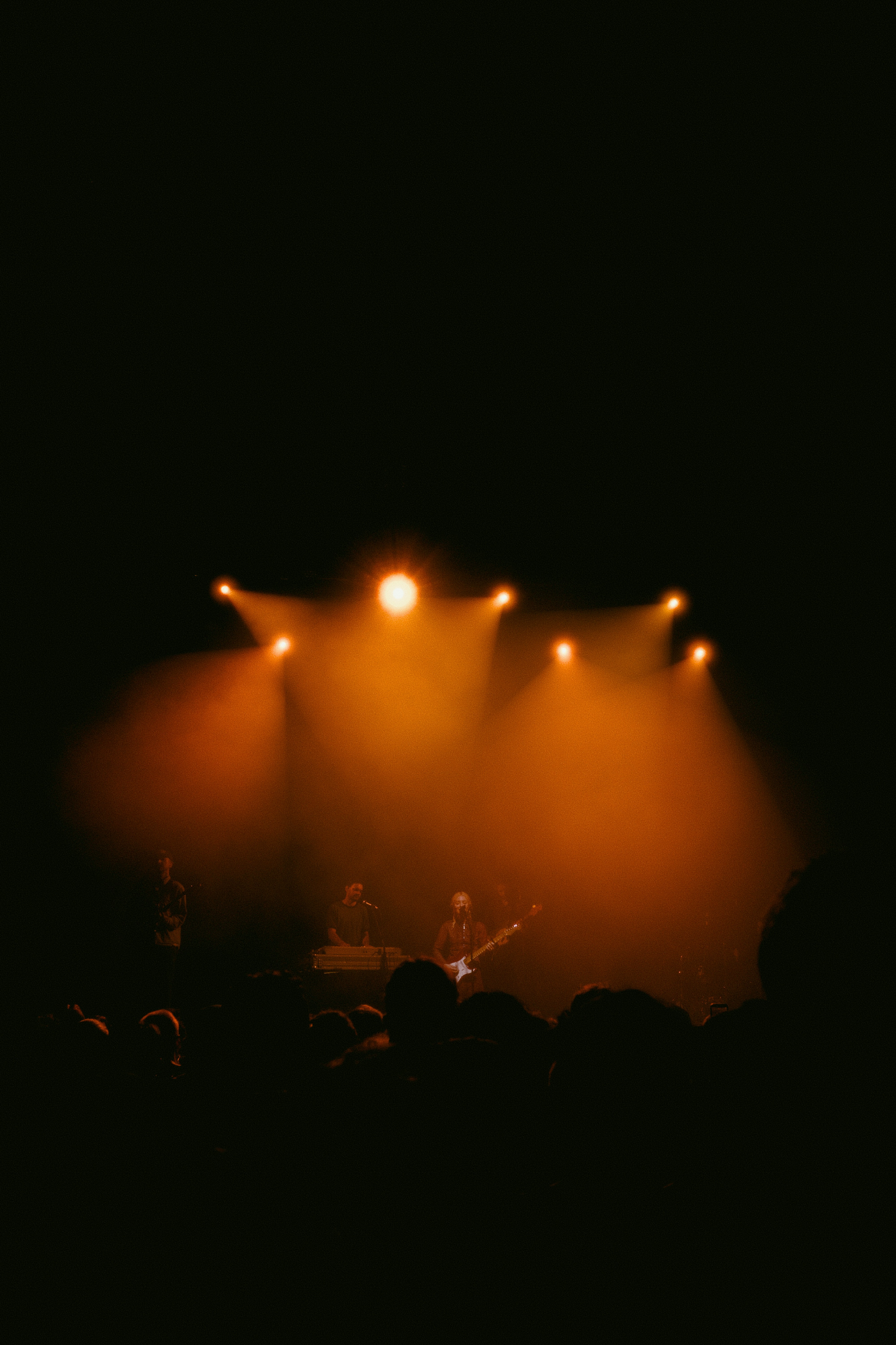 Audience watches musicians perform on stage under orange spotlights.
