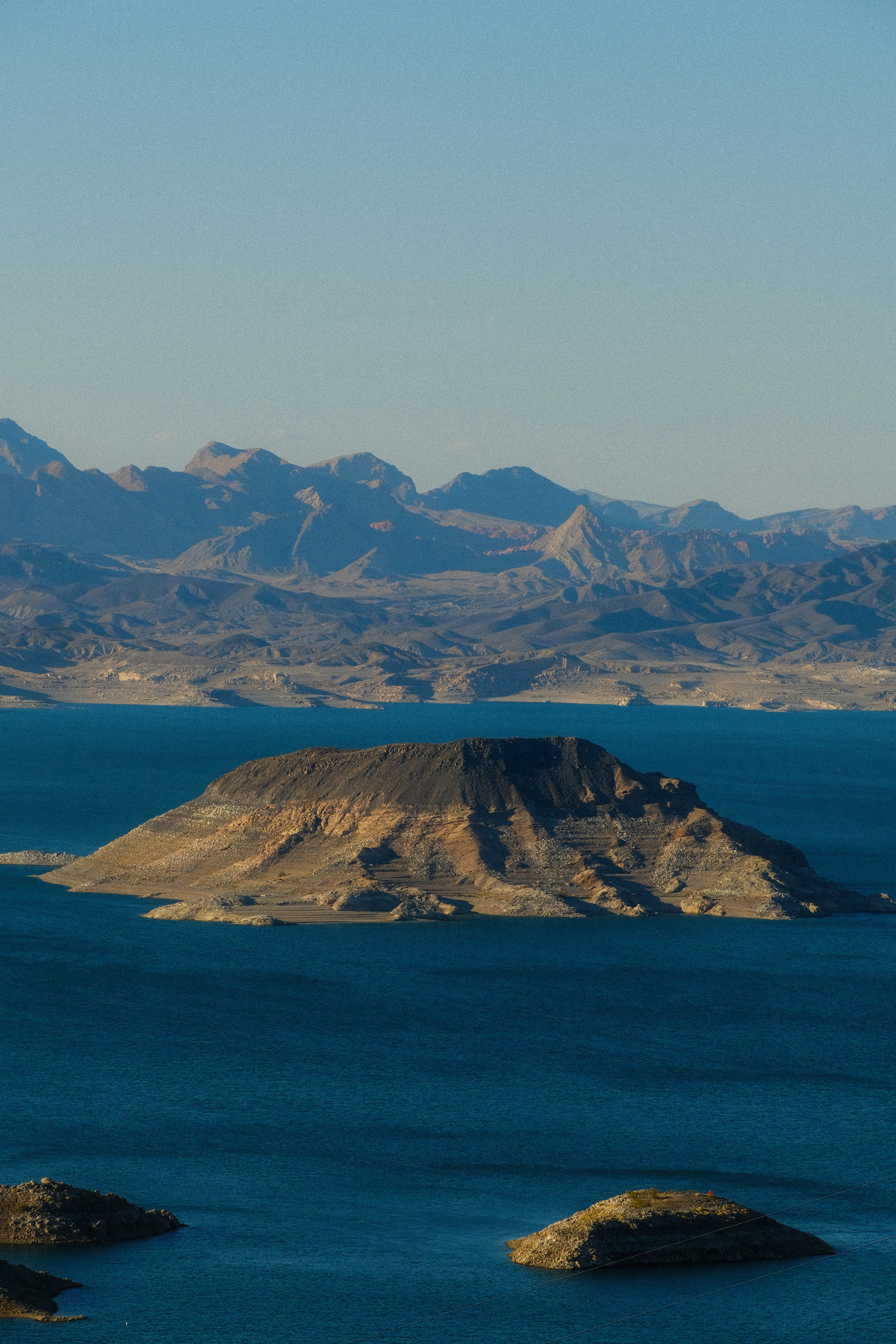 Isola arida in un lago blu con montagne lontane.