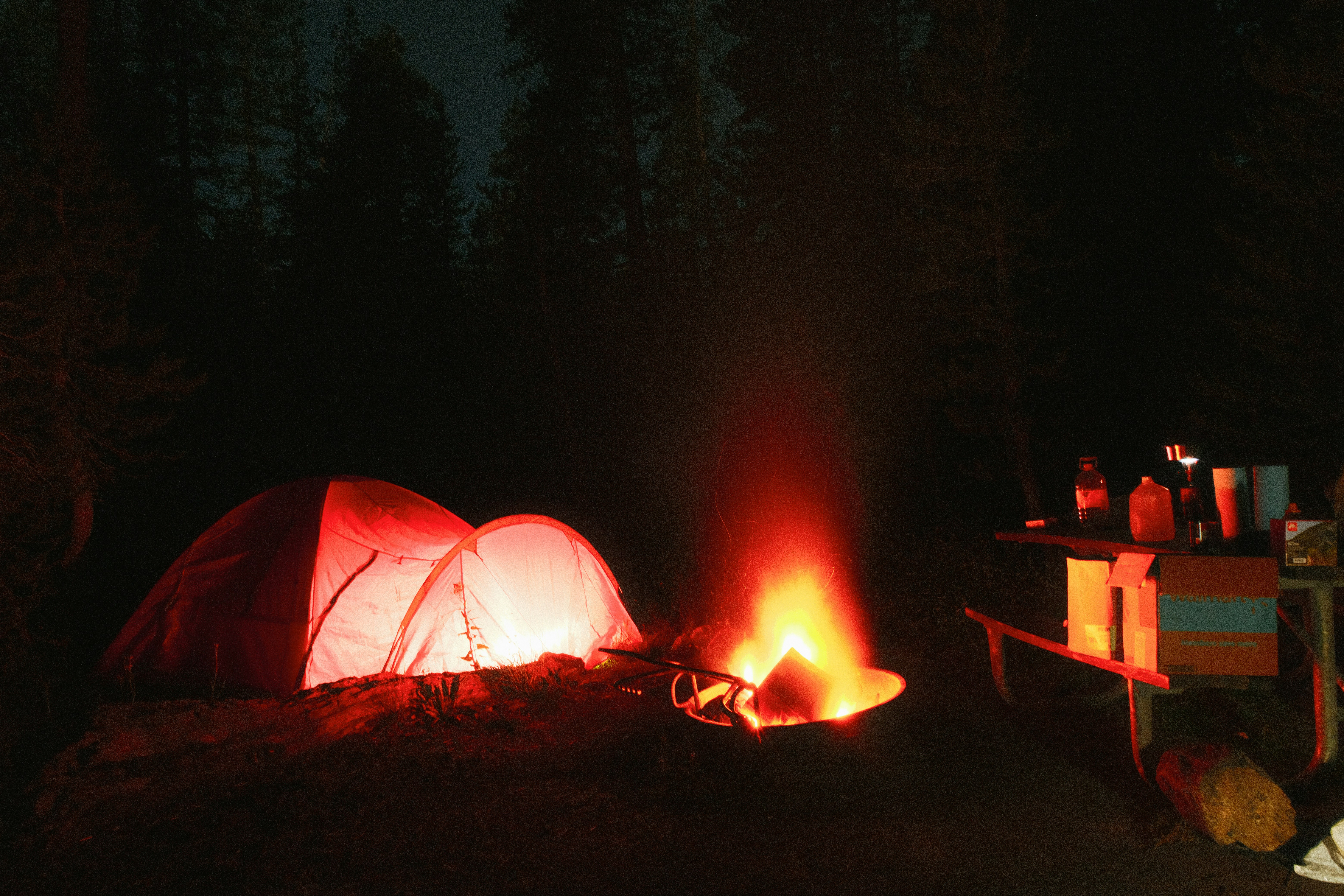 Una tenda luminosa e un falò illuminano un campeggio scuro nella foresta.