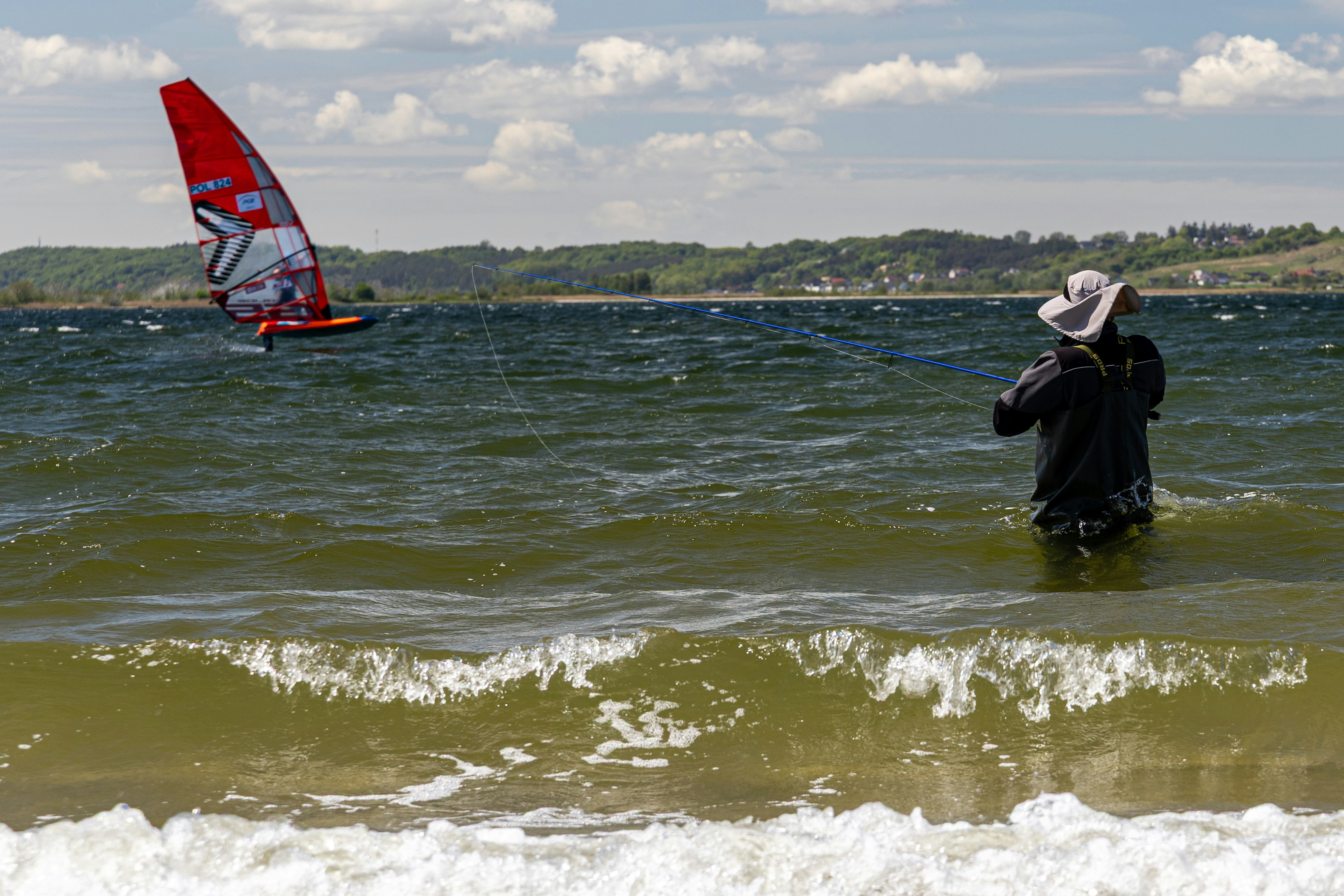 Una persona in acqua osserva un windsurfista con una vela rossa