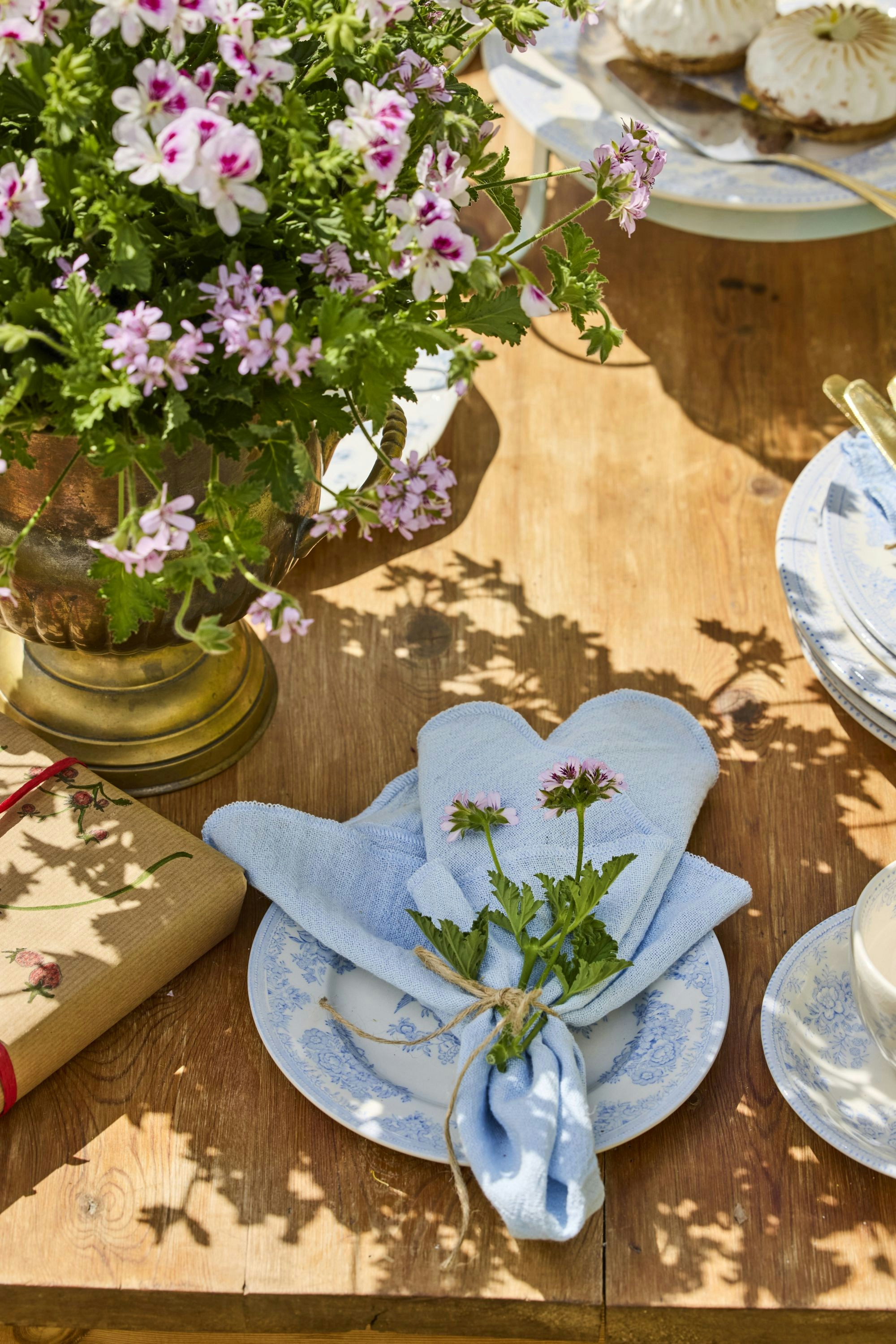 Elegant outdoor table with pink flowers, gift, and blue napkin