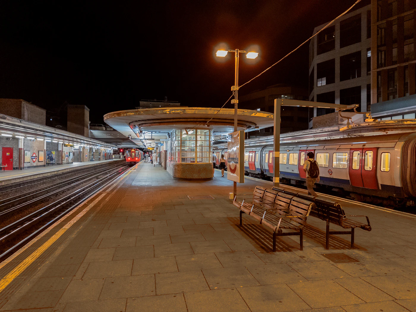 A railway platform at night with benches and a waiting train