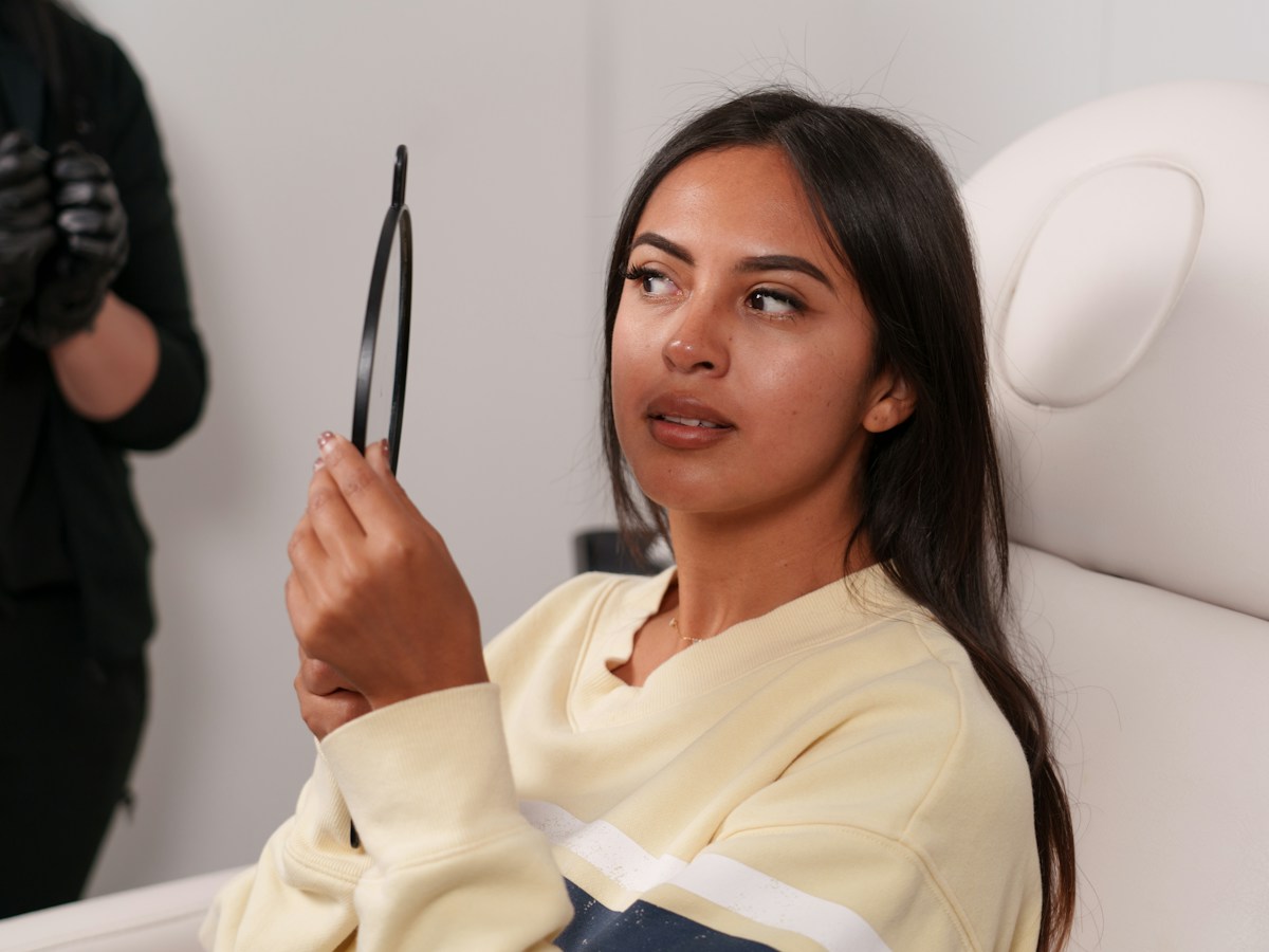 Clienta sentada en el sillón de un centro de estética mirándose en un espejo de mano