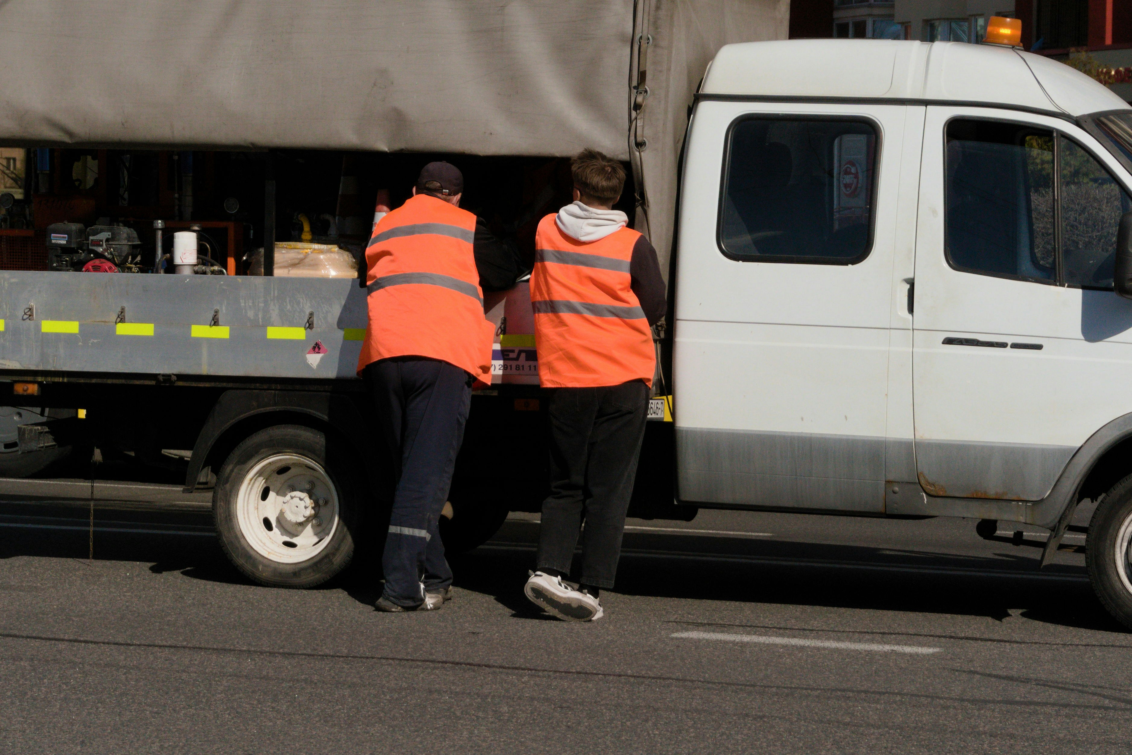 Zwei Personen in orangefarbenen Westen stehen bei einem weißen Truck.