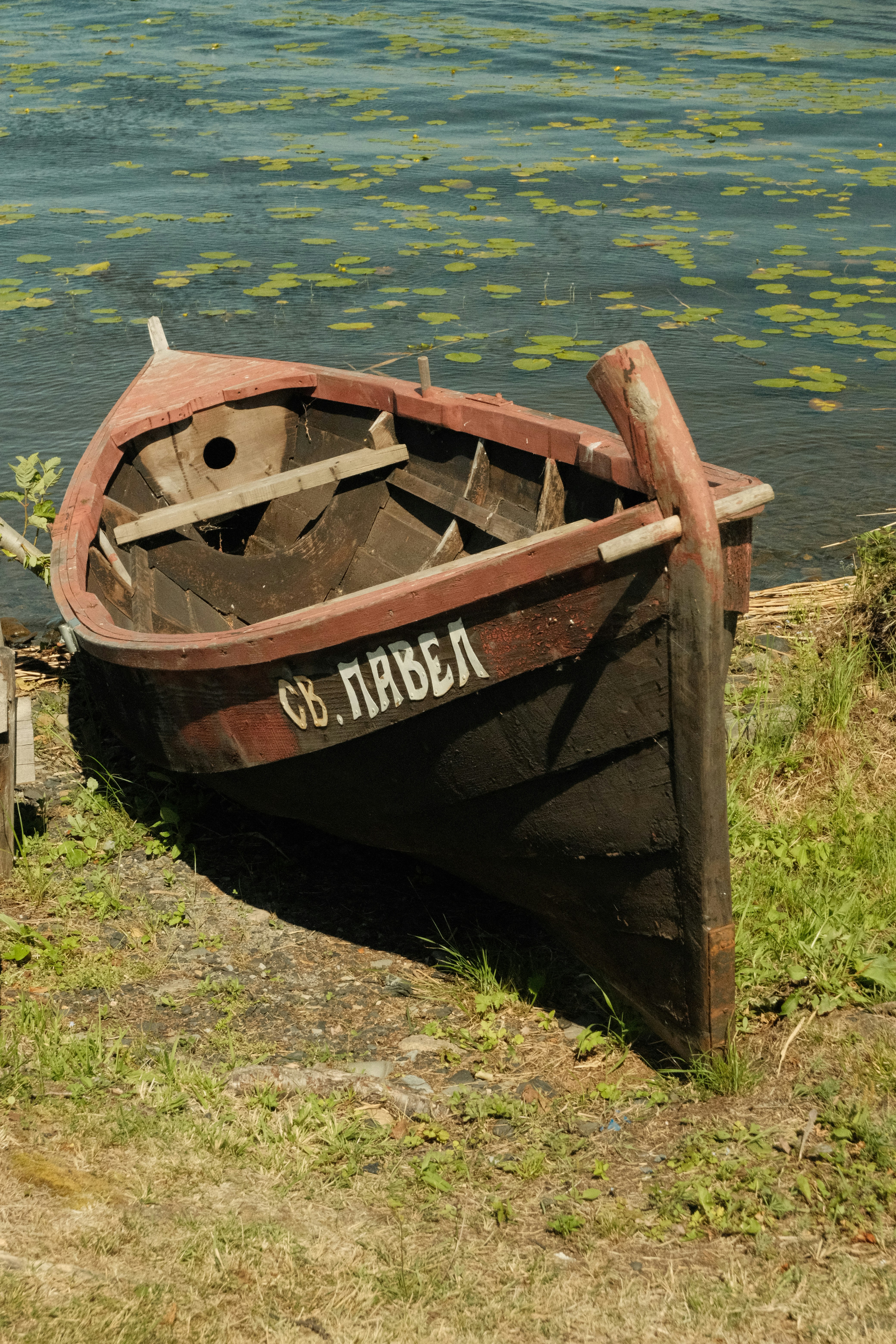 Old wooden boat named "св. павел" on grassy bank.