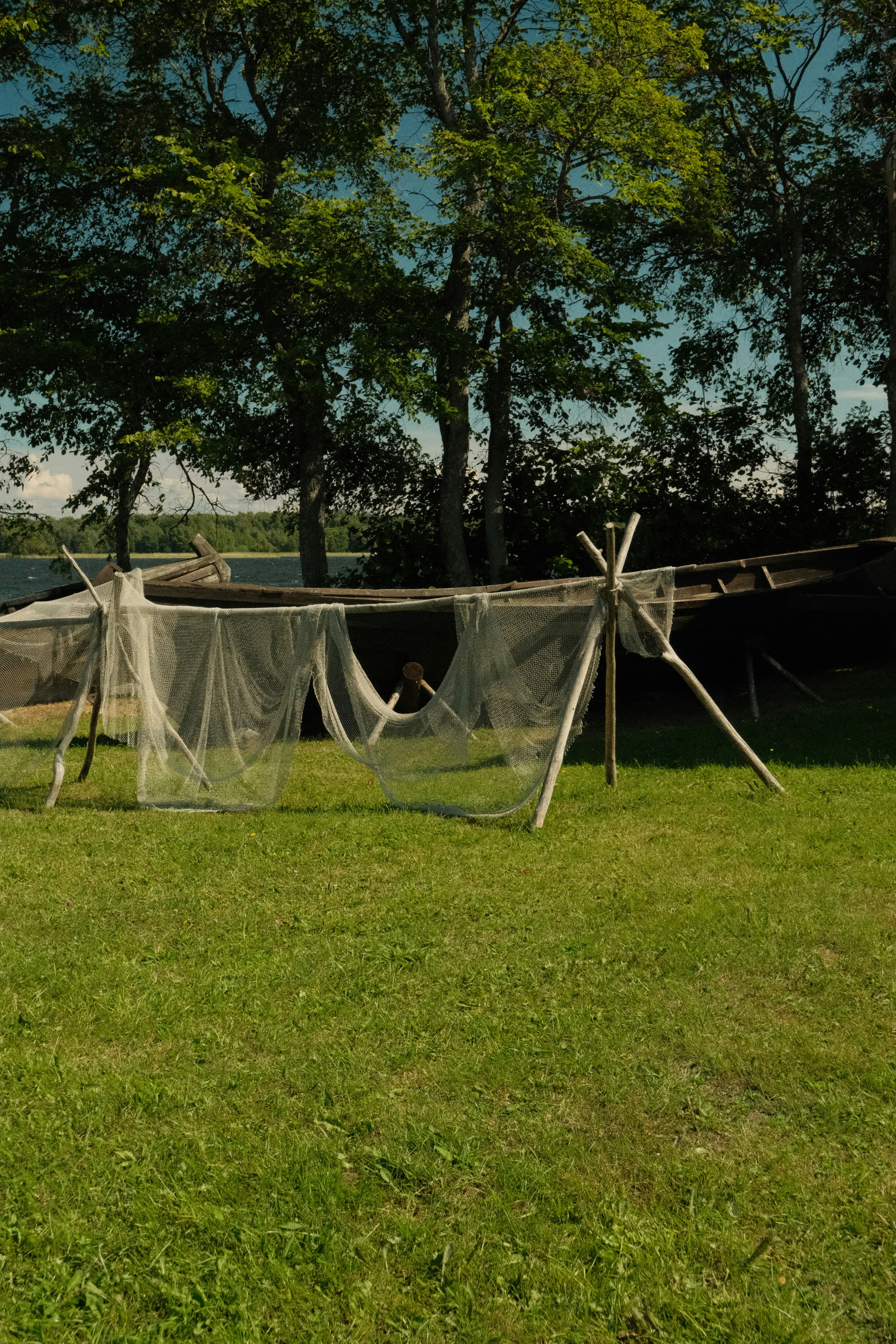 Rustic wooden frame with netting on green grass by water.